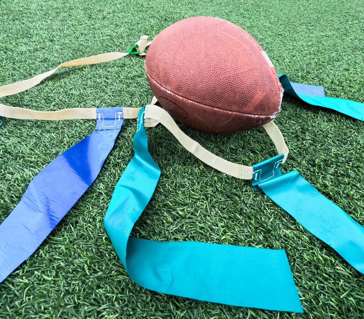 Sports equipment for flag football play. White belts with green and blue flags. Football in the center of view. Green football field turf background.