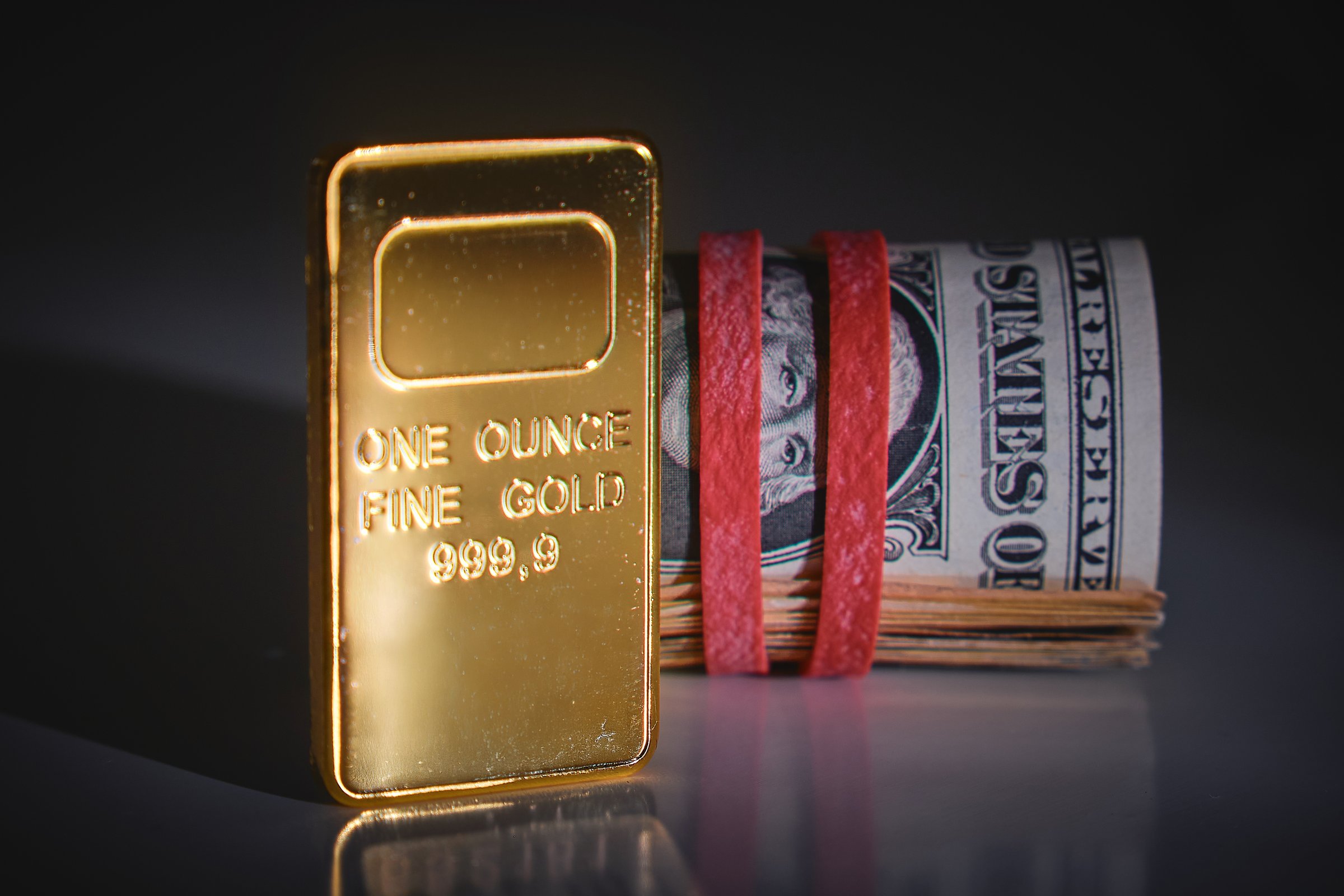 Gold bar standing next to rolled us dollar bills tied with red elastic bands