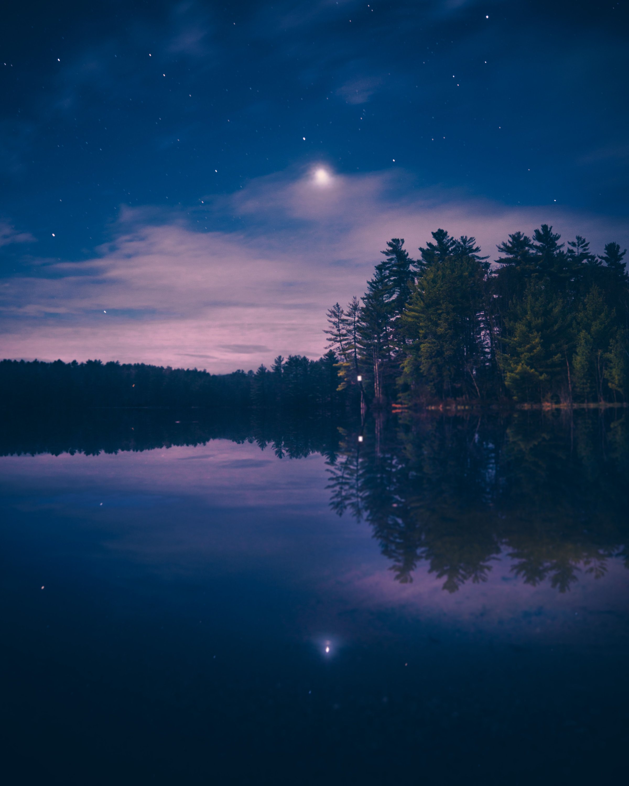 A serene night landscape with a starry sky reflecting on a calm Maine lake surrounded by pine trees.