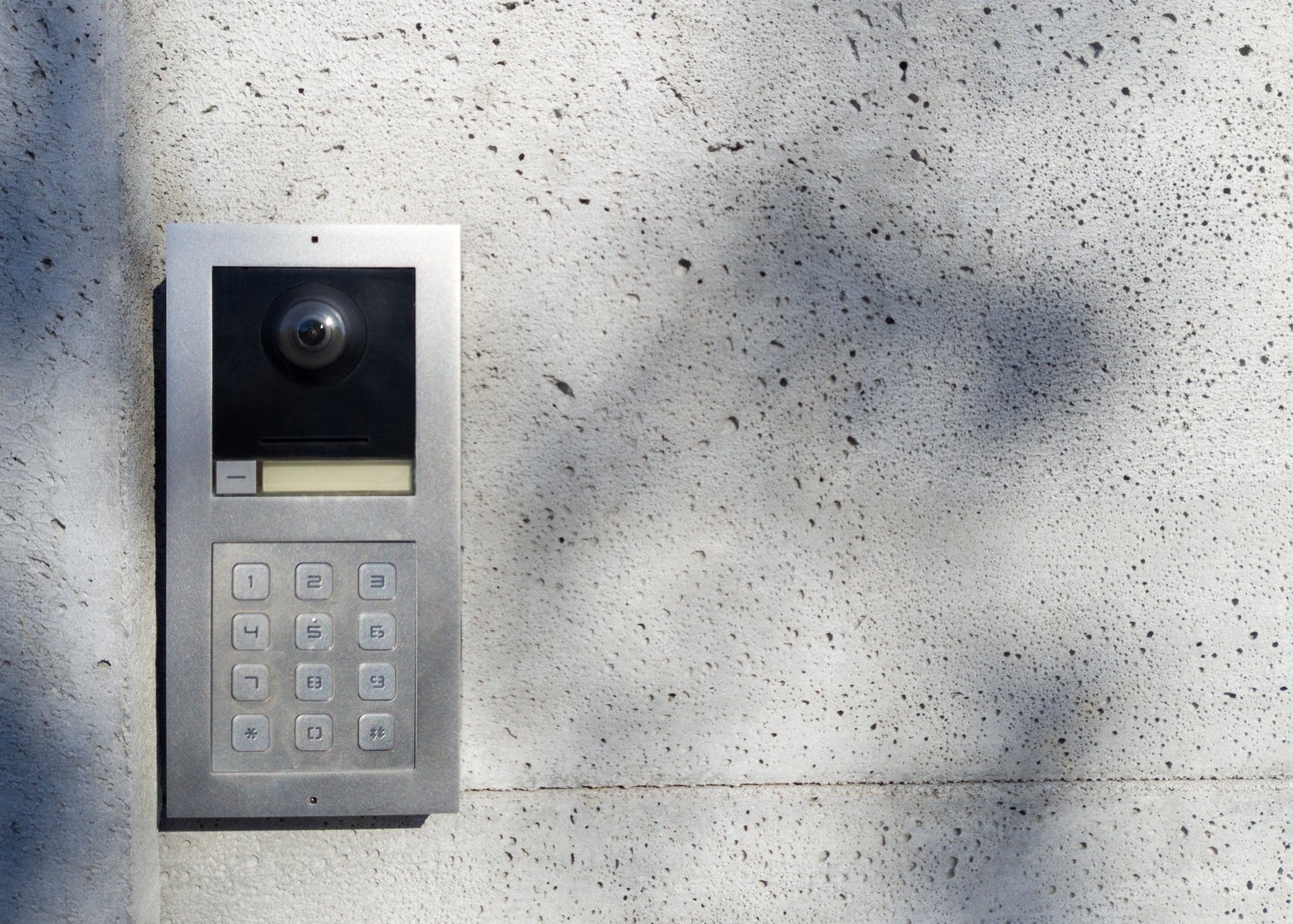 Close up of a metal intercom with a keypad mounted on a modern concrete wall in natural light