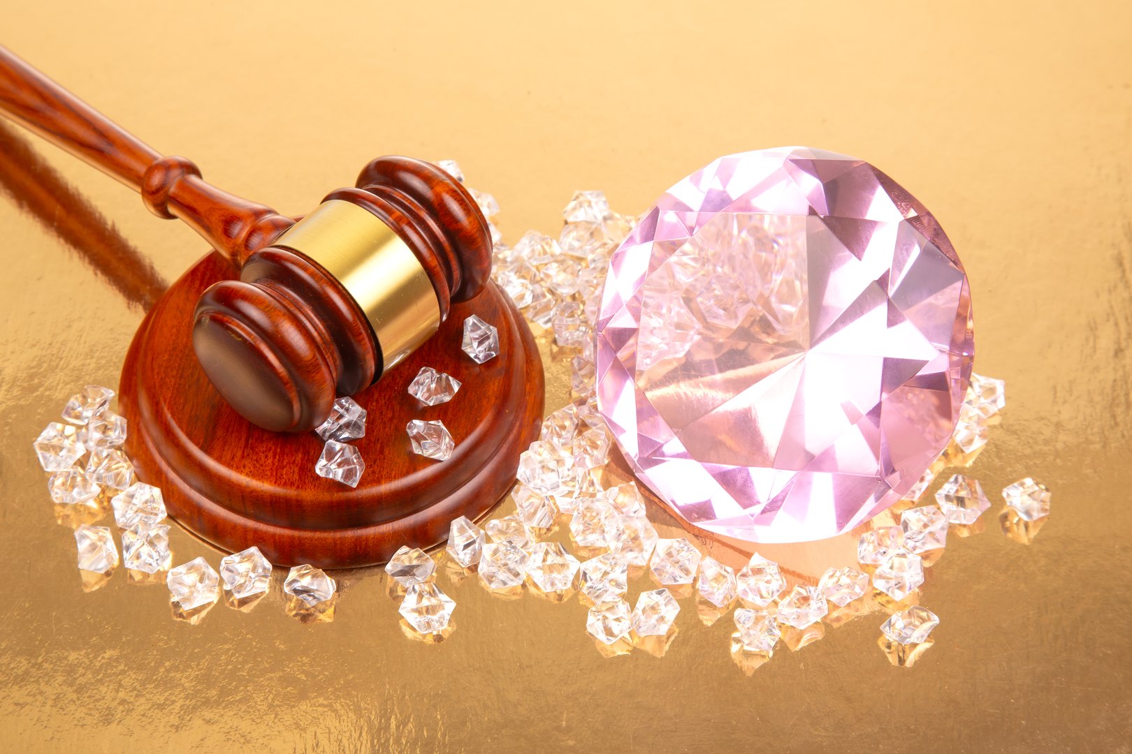 A gavel is placed next to a large pink gemstone along with smaller clear diamonds. This setting evokes the excitement of an auction, showcasing valuable items under bright lighting.