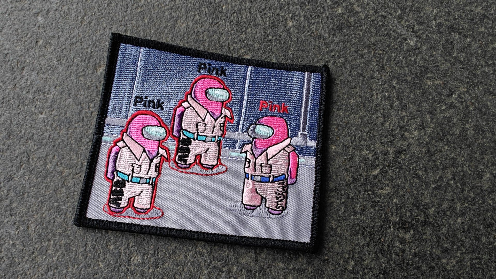 Patch with three cartoon astronauts in pink spacesuits on a gray background, labeled Pink above each figure.