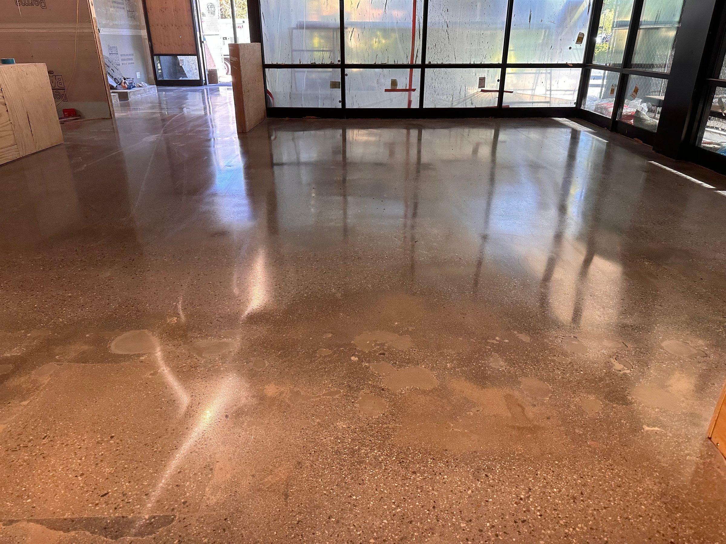 A shiny, polished concrete floor in a room with large windows and partially completed construction work visible.