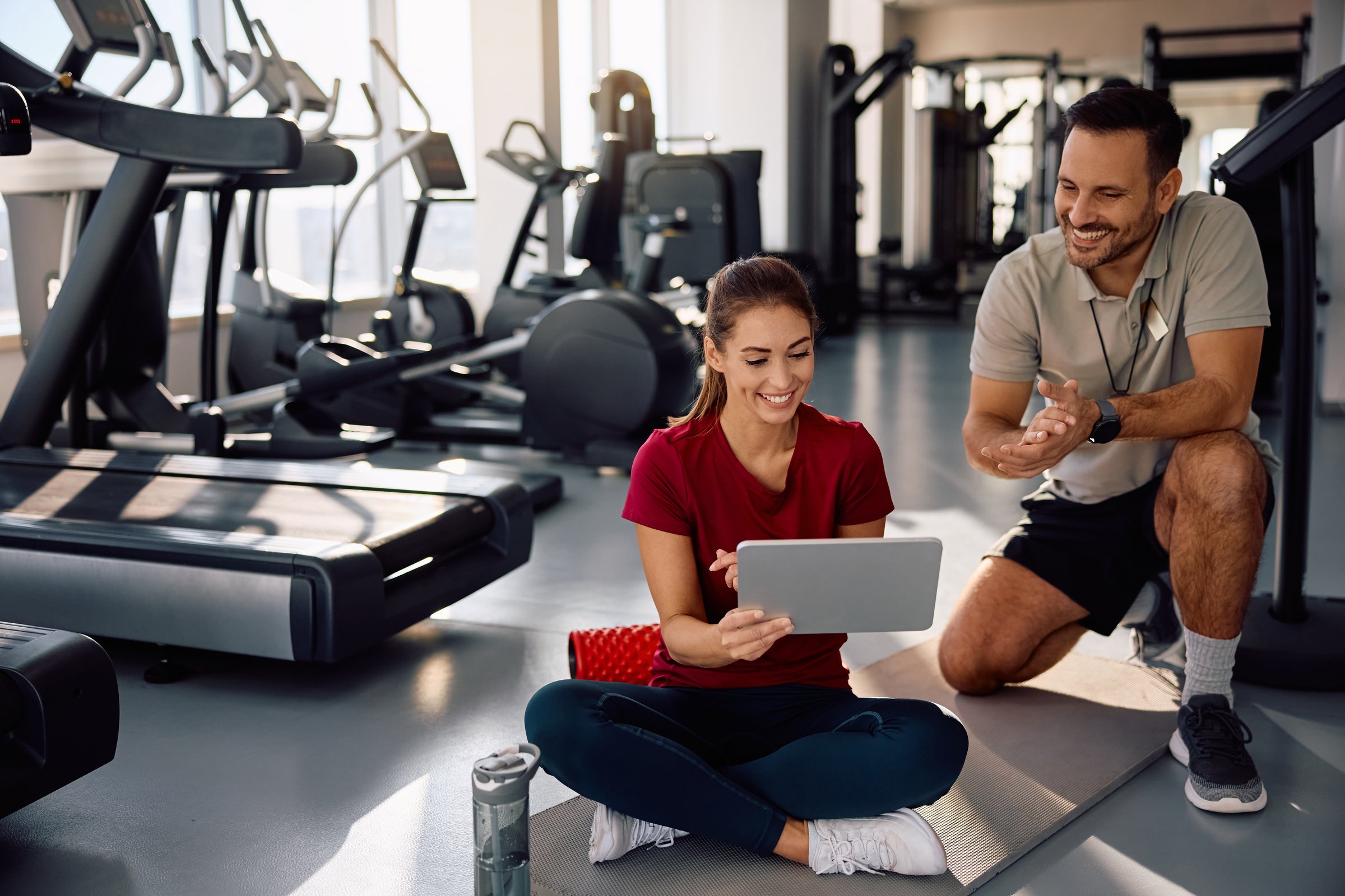 Young happy athlete and her personal coach during touchpad during exercise class at health club.