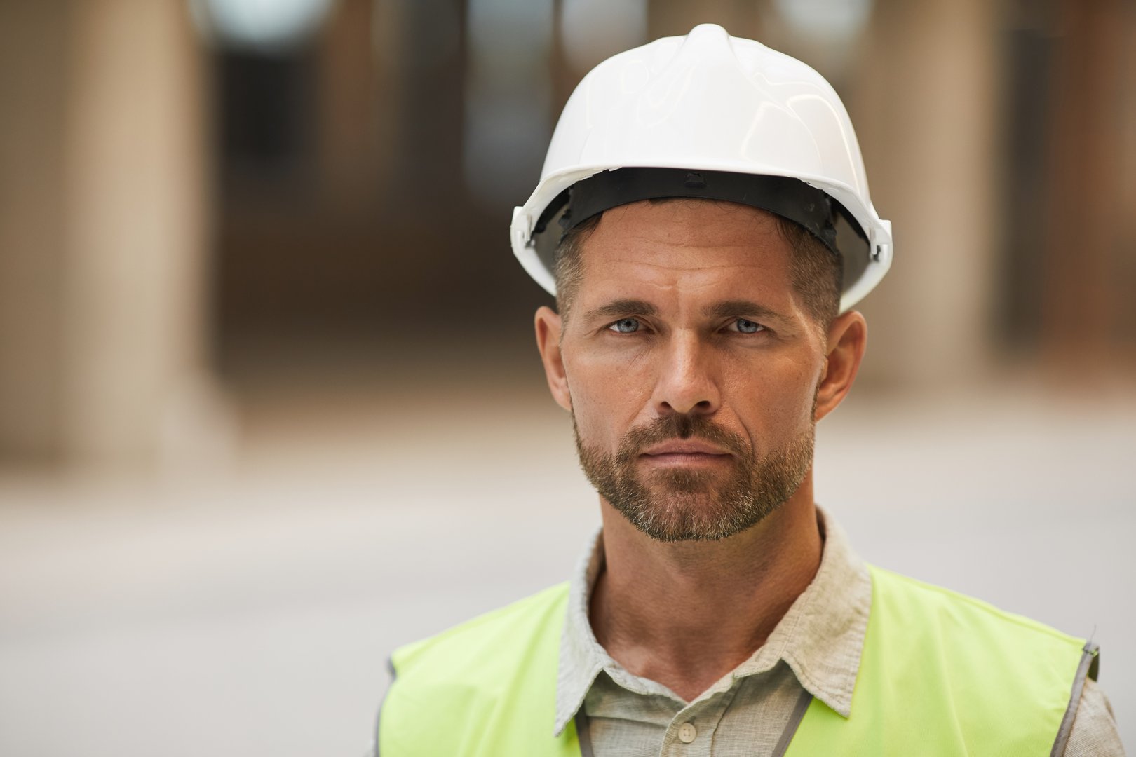 Close up portrait of mature construction worker wearing hardhat and looking at camera while standing at construction site, copy space