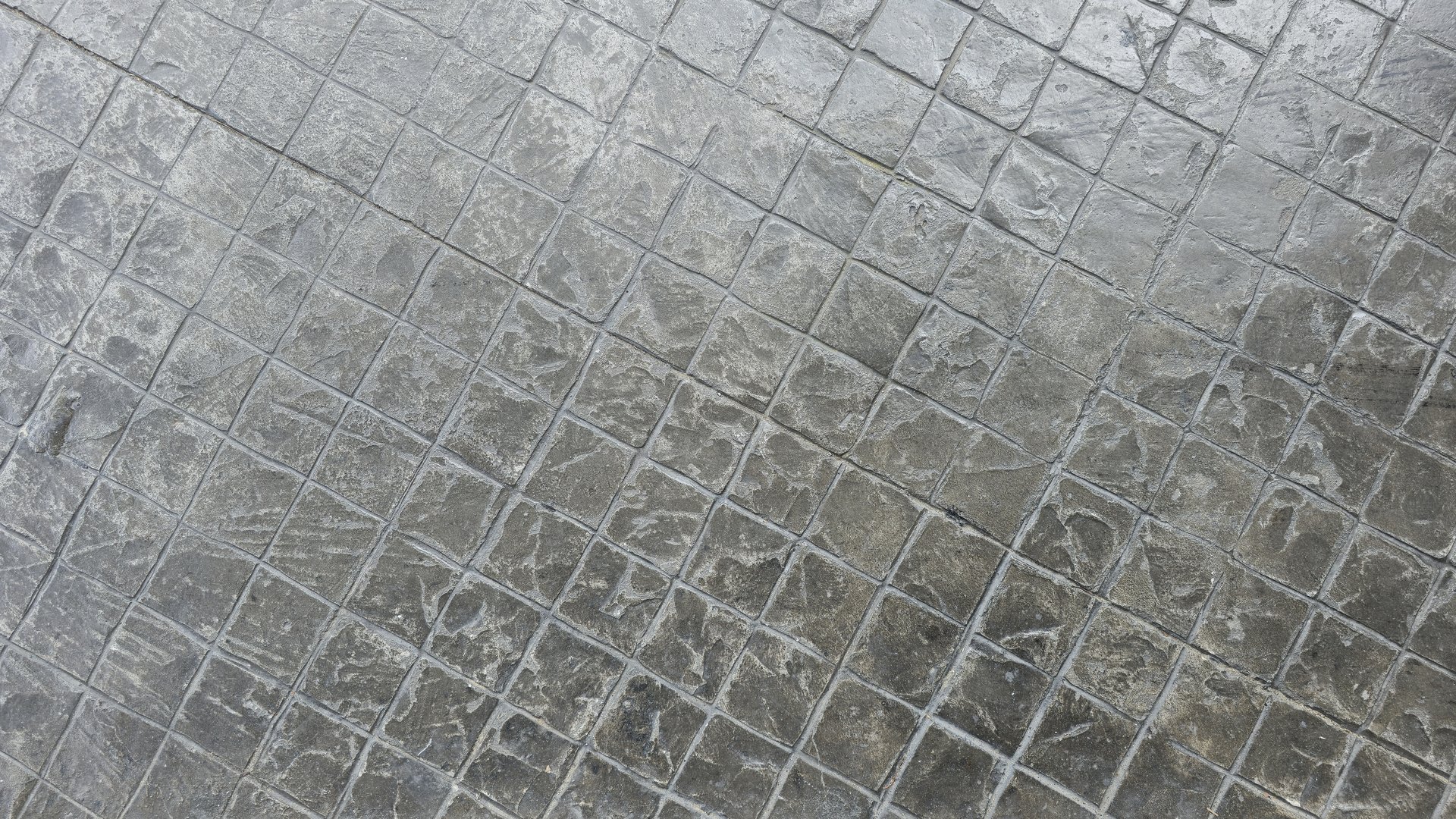 Stamped concrete background with a stone-like grid pattern. The matte gray surface includes visible grooves, light scratches, and tonal depth that emphasize the realistic stone texture.