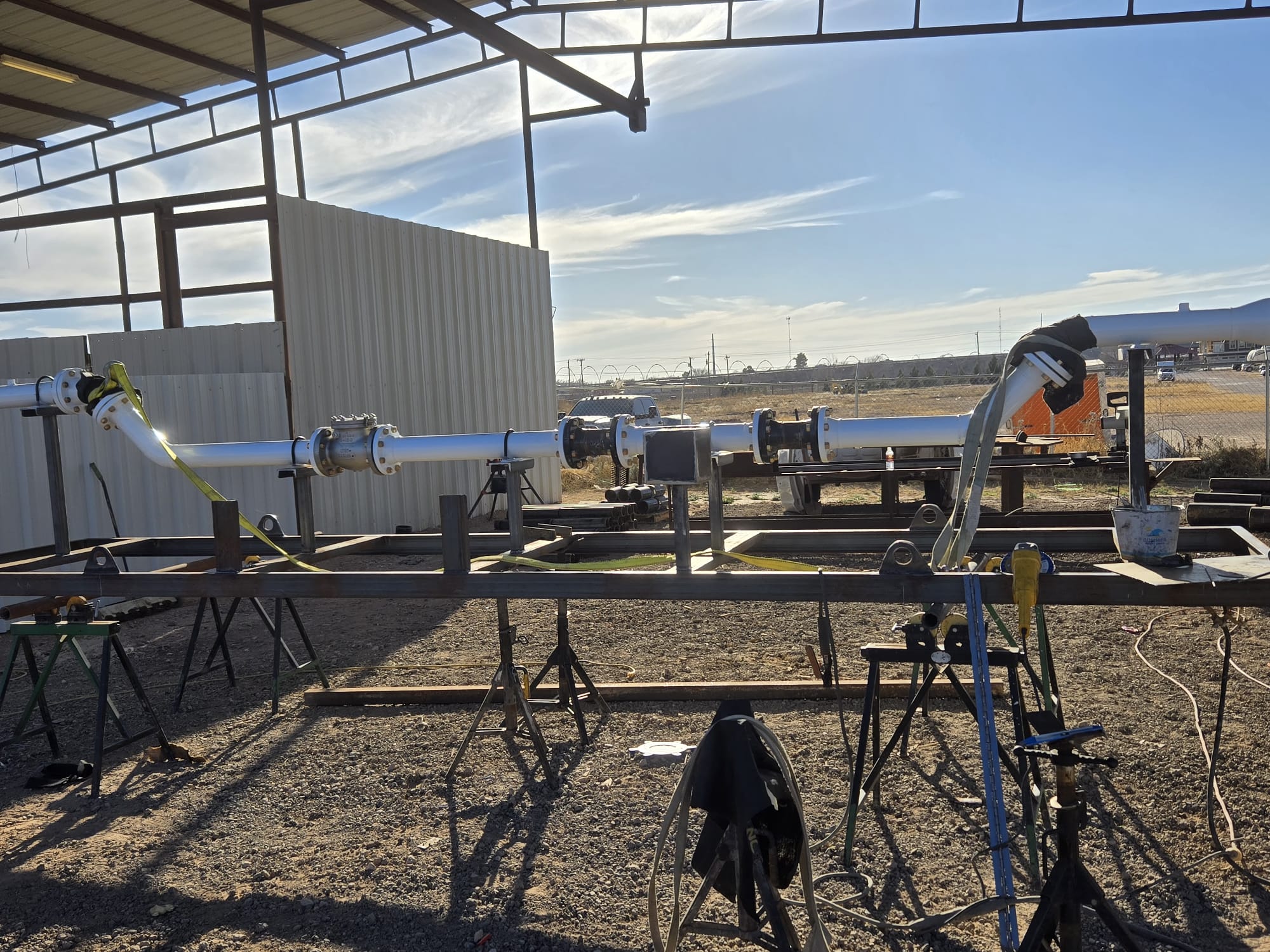 Large metal pipes with flanged connections mounted on steel supports in an outdoor industrial setting with clear skies.