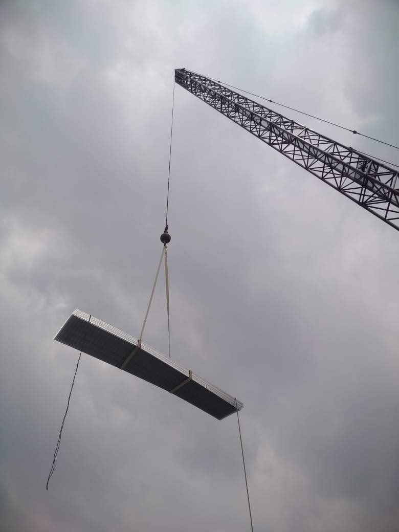 Crane lifting a large metal beam against a cloudy sky.