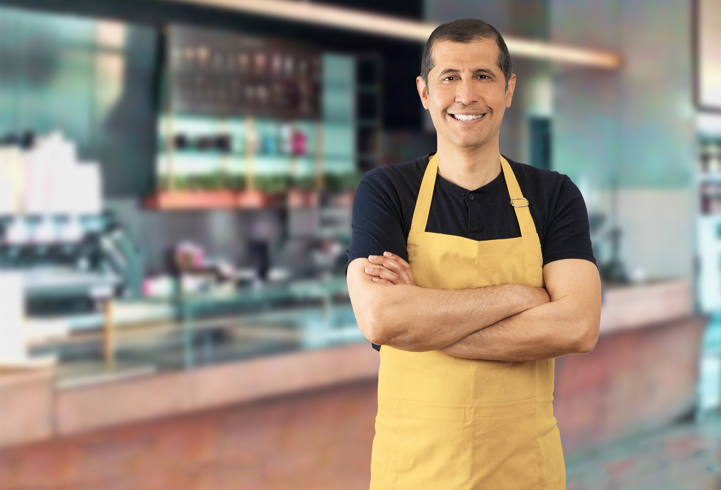 Portrait of a confident man with yellow apron standing at coffee shop