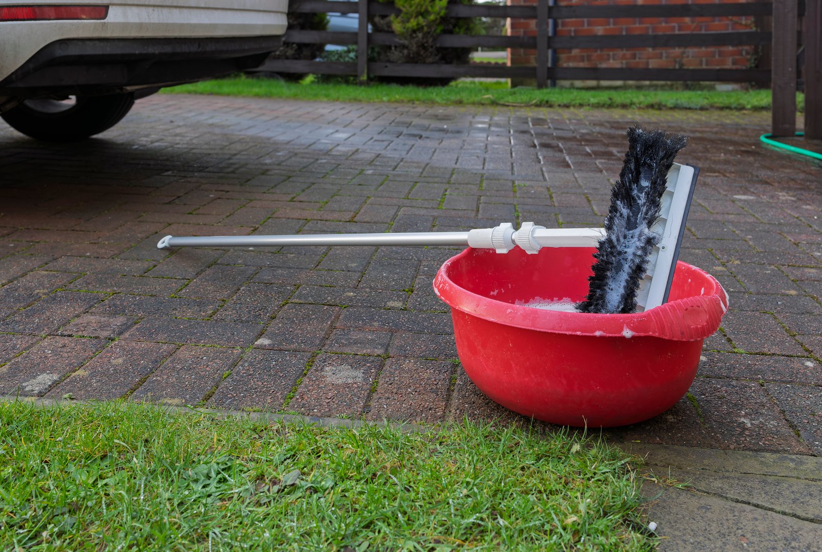 Soapy Brush and Squeegee on Silver Pole and Red Bowl for Car Washing on Home Driveway