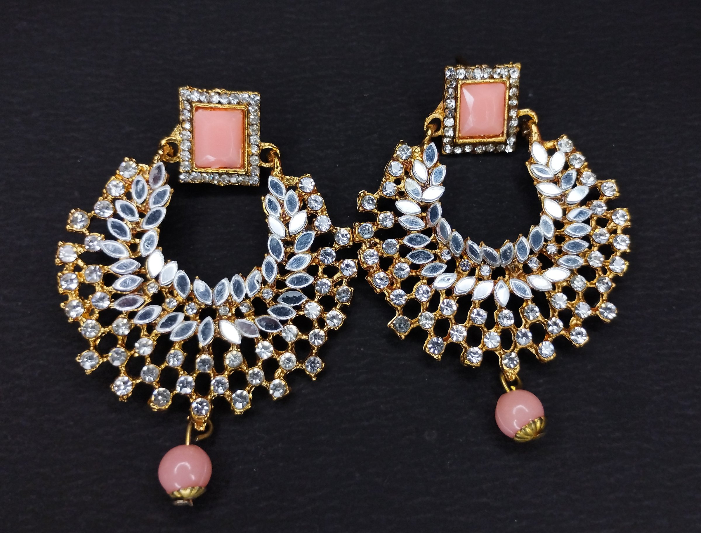 A pair of stunning designer kundan earrings featuring intricate stonework, a square pink gemstone stud, dazzling white kundan embellishments, and a delicate pink bead drop. These traditional Indian earrings are crafted with golden polish, making them perfect for weddings, parties, festivals, and ethnic wear. Elegant and timeless, they add charm and sophistication to any outfit, ideal for women and girls who love statement jewelry.