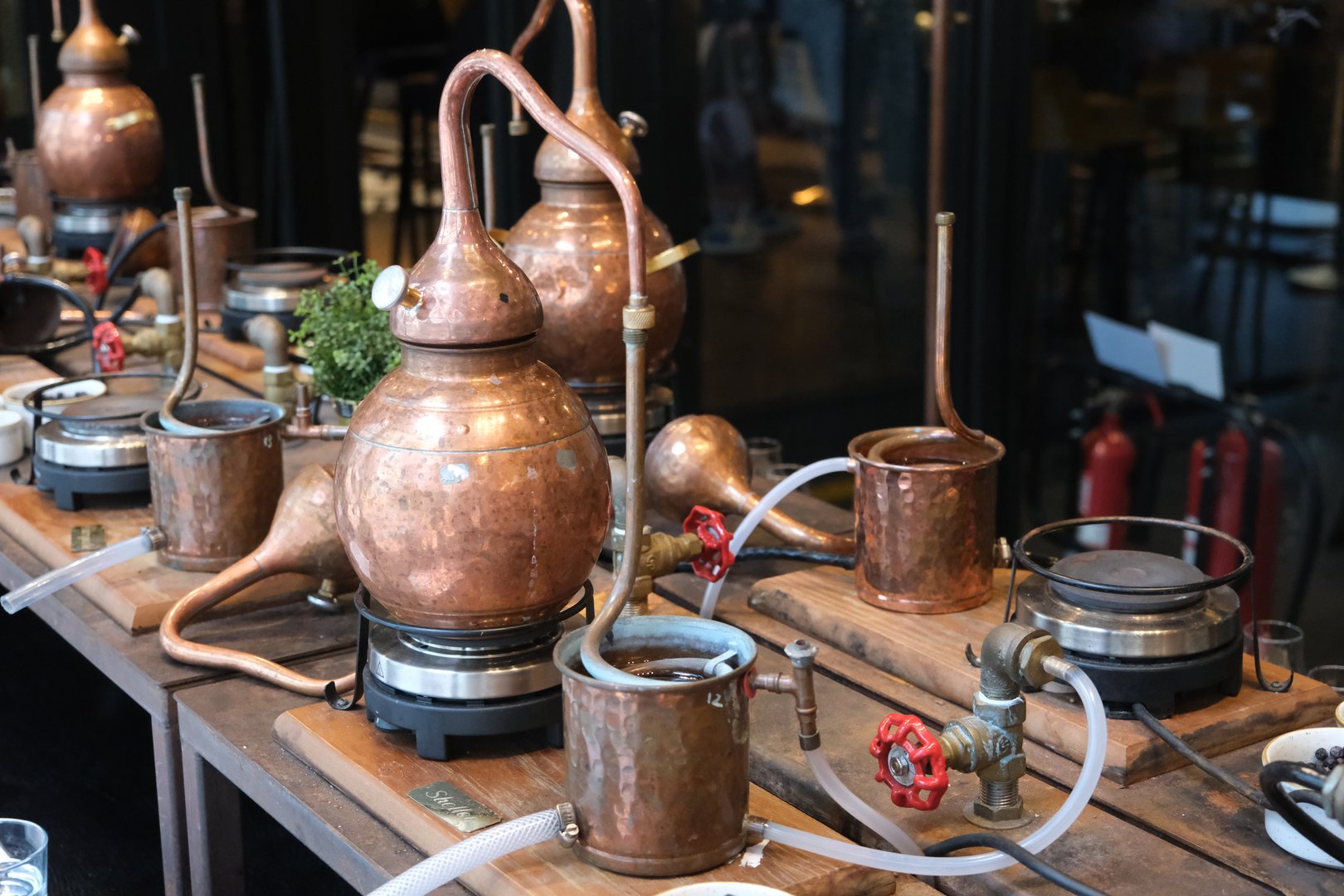 Small copper stills and distilling equipment arranged on a decorated table.