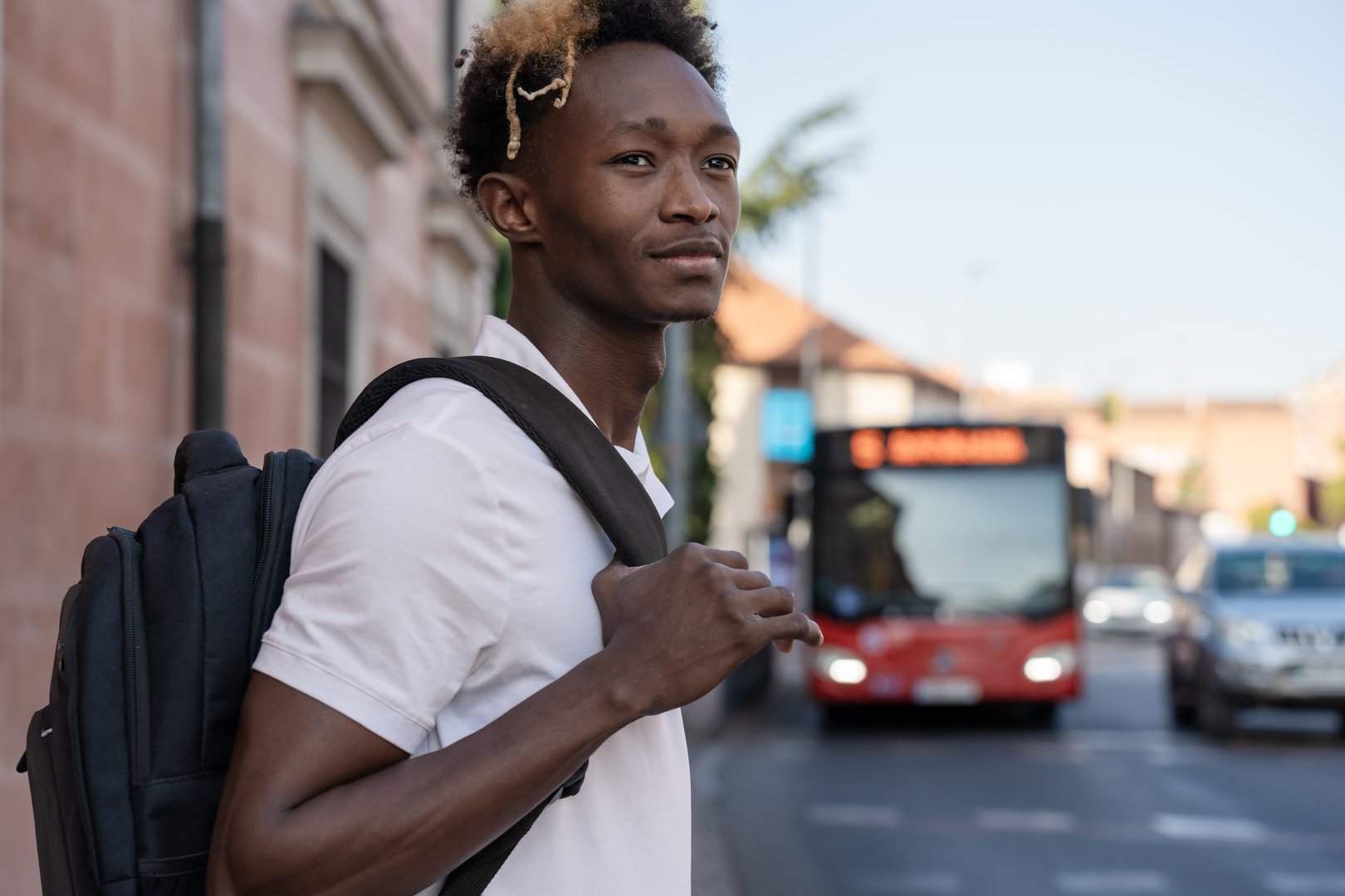Young college student is holding his backpack strap while waiting for the bus