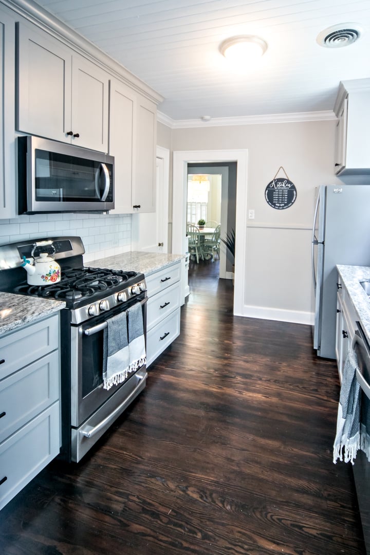 A small cottage kitchen with gray cabinets and dark hardwood floors in a short-term rental house.