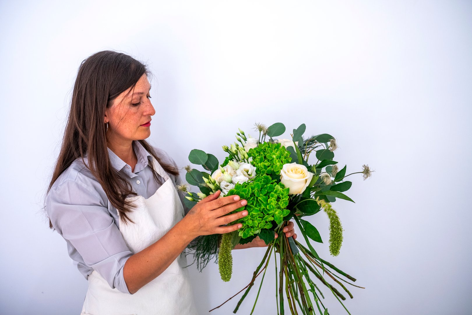 Woman florist arranging a fresh, elegant bouquet of white roses and green hydrangeas for a special occasion or delivery service