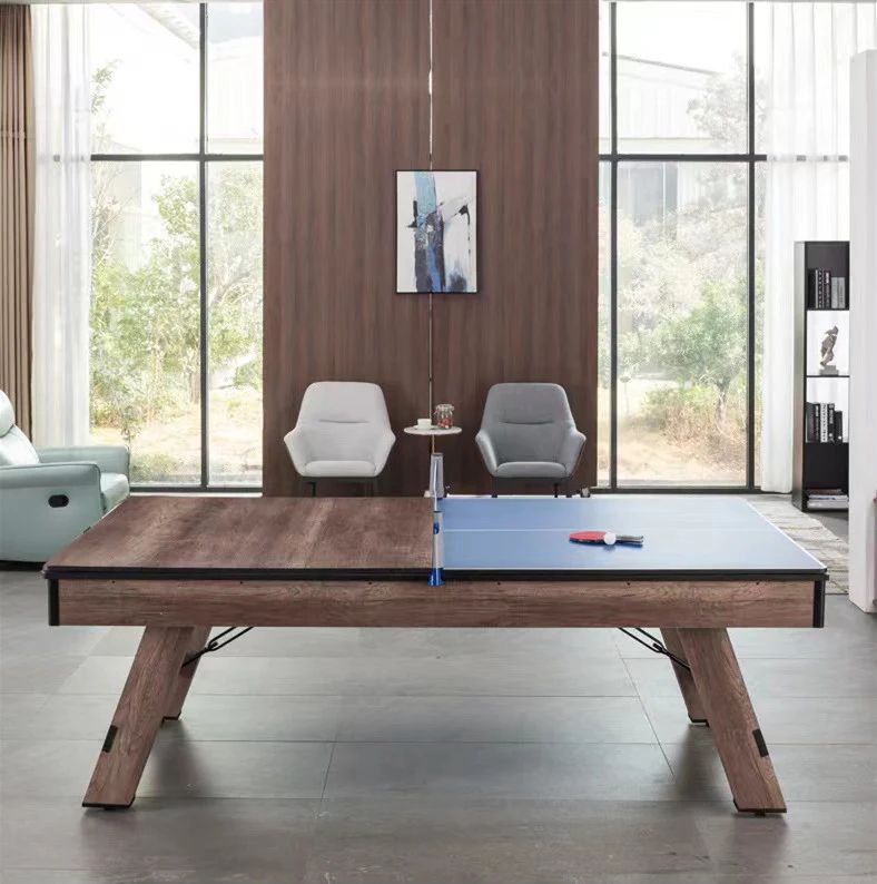 A table tennis table with a net and paddles in a modern room with chairs, a small table, and a large window.