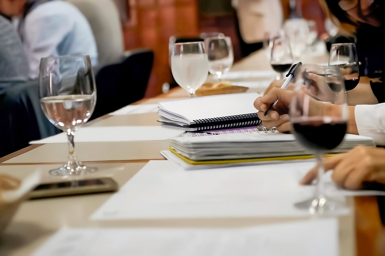Sommeliers are evaluating wine during professional tasting session, taking notes on flavors, aromas, and characteristics in notebooks on table with glasses of wine