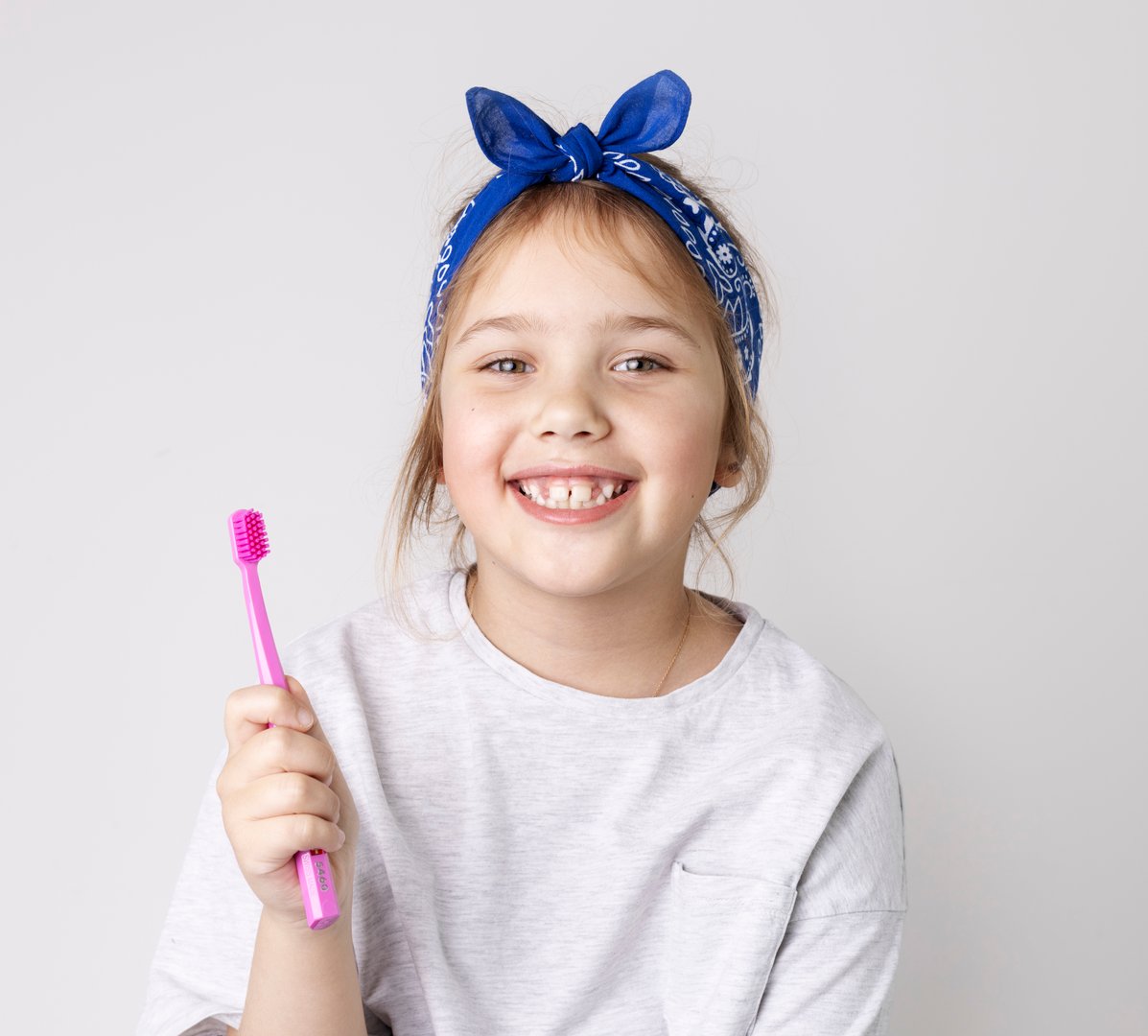 Child girl holding tooth brush smiling face on grey background. Caucasian kid dental concept.Stomatology.Cute toddler.