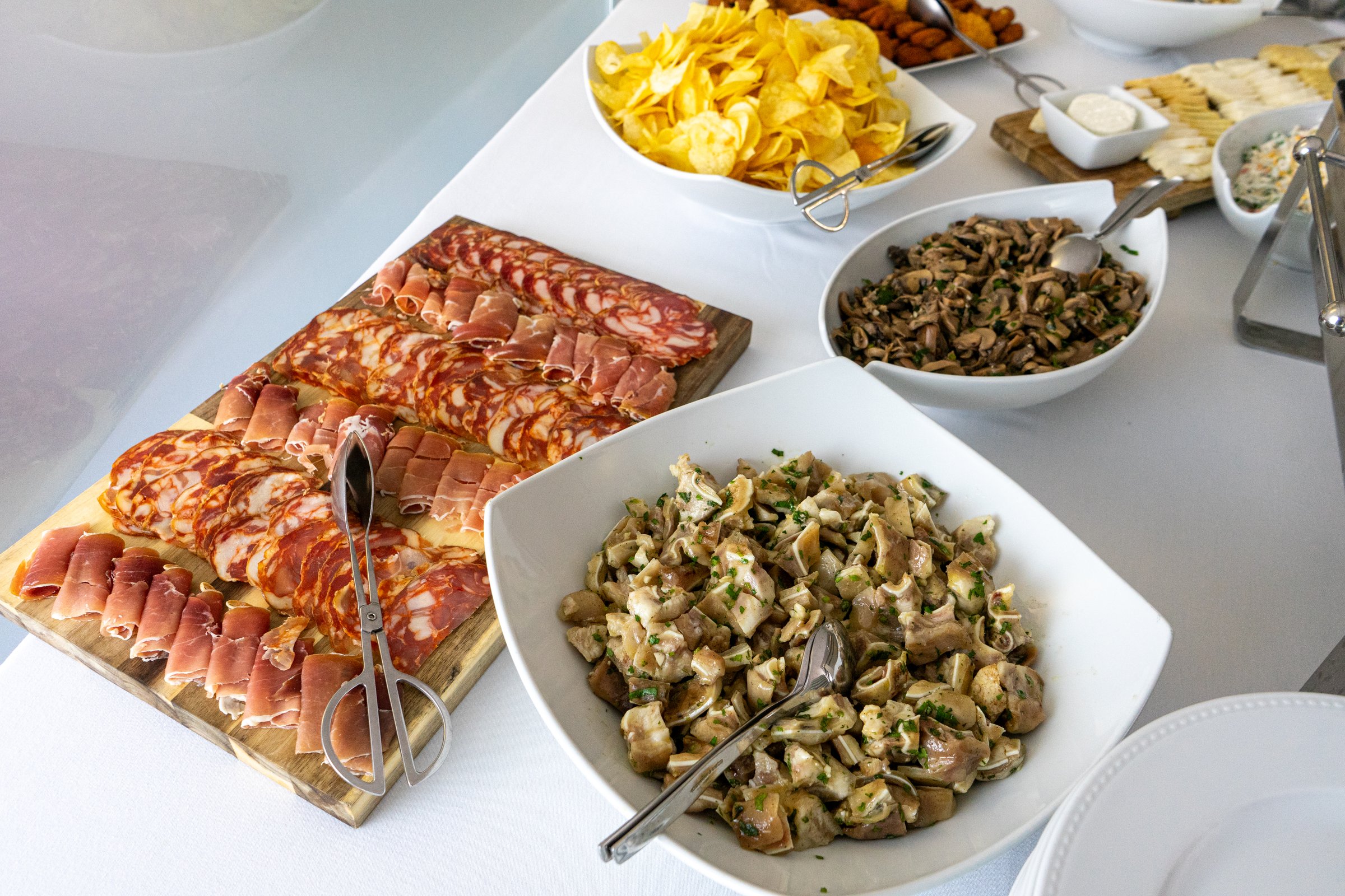A beautifully arranged hotel buffet featuring savory sliced paio, cured ham, sautéed mushrooms, pork ear with coriander, and crispy fries, showcasing a feast of flavors.