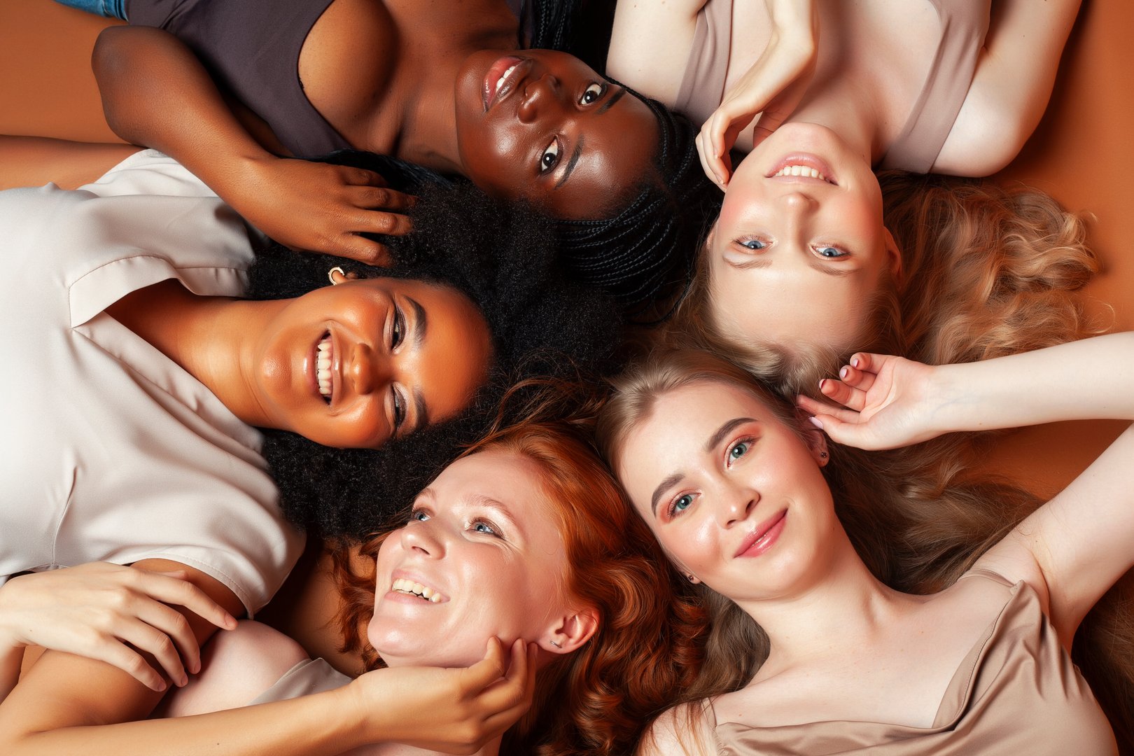 young pretty african and caucasian women posing cheerful together on brown background, lifestyle diverse nationality people concept closeup