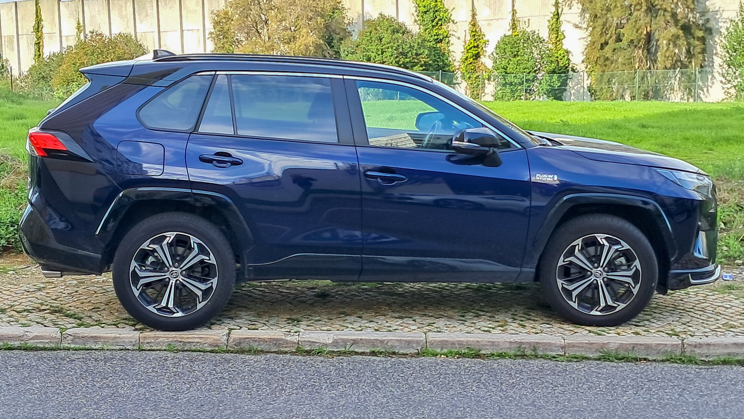 Lisbon, Portugal, September 16, 2024, Side view of a brand new dark blue toyota rav4 plug in hybrid parked on a sidewalk near a green lawn