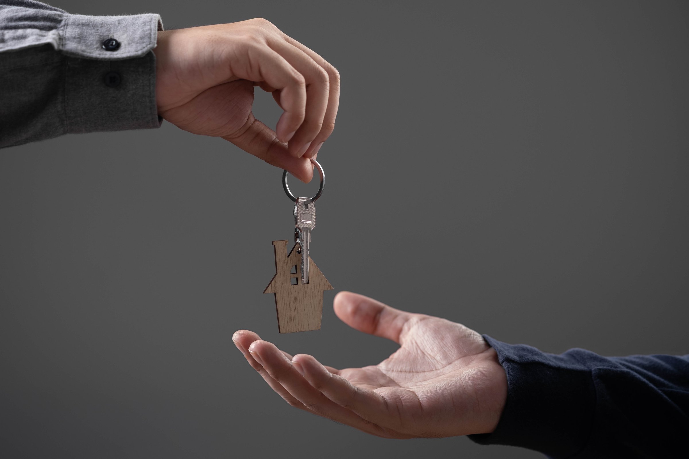 Close-up of hand giving house key to another person, symbolizing home ownership, real estate transaction, or property rental. Ideal for housing, mortgage, or investment concepts.