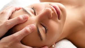 A person receiving a relaxing facial massage, with hands gently pressing on their forehead. The person has a serene expression.