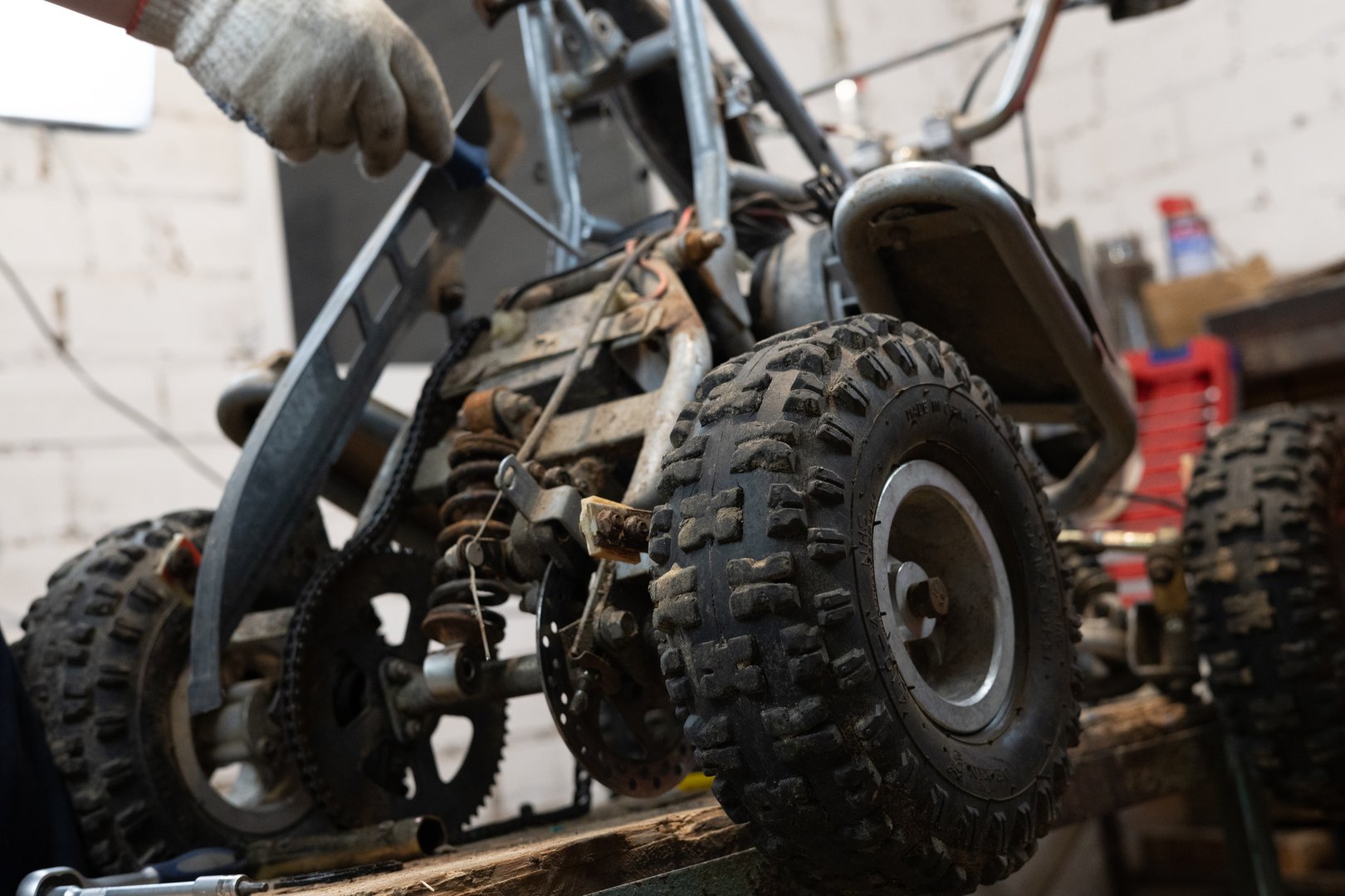 A man finishes repairing an ATV in his garage. A man repaired his son's little red four-wheeler in his garage and replaced the broken parts with new ones. Broken quad bike concept..