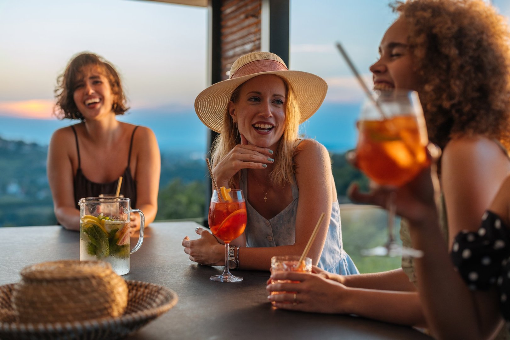 Three women laughing and enjoying cocktails together on a panoramic terrace bar