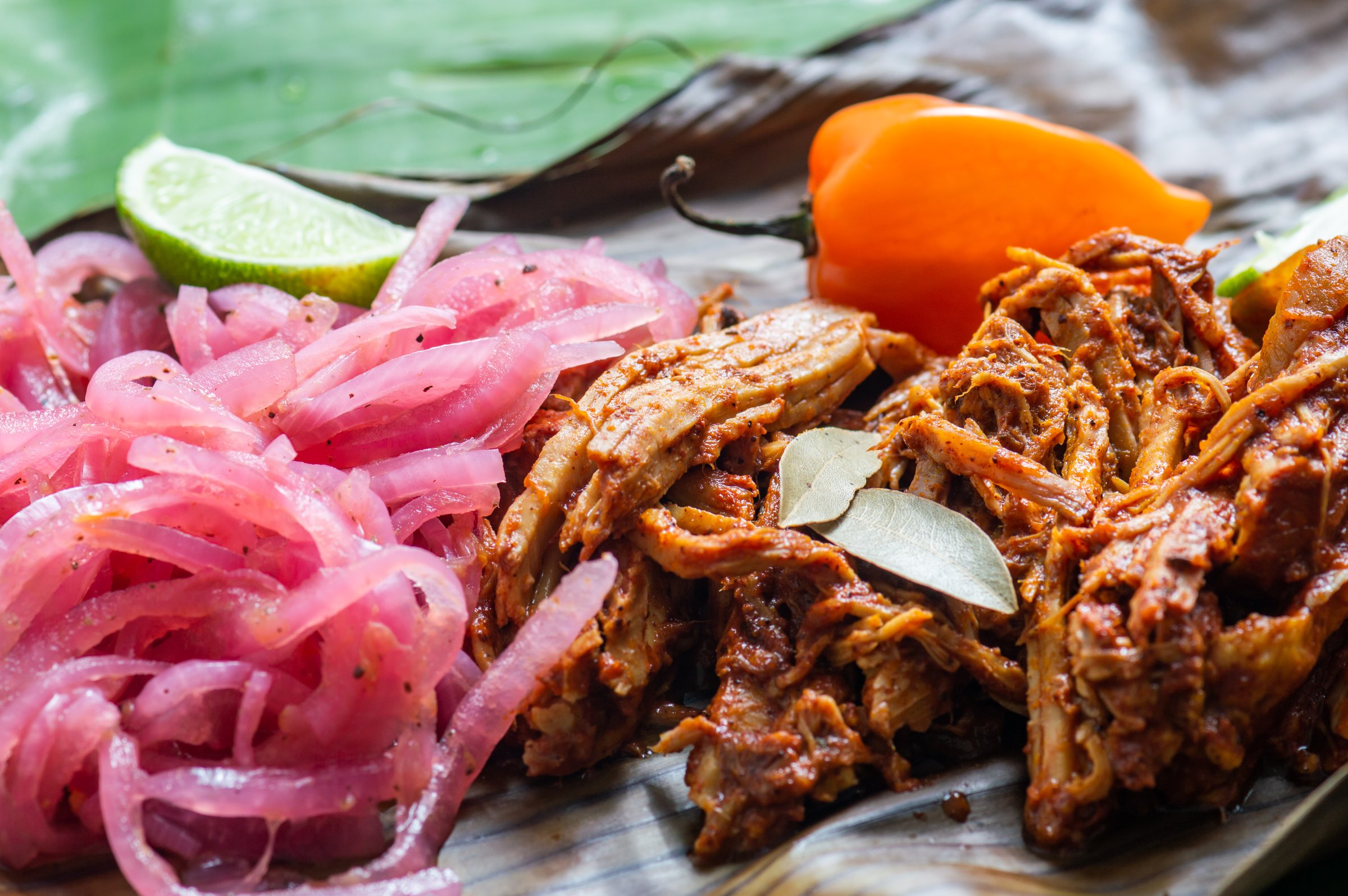Cochinita Pibil, Mexican pit-roasted pork dish from Yucatan peninsula, served on banana leaves with traditional condiments