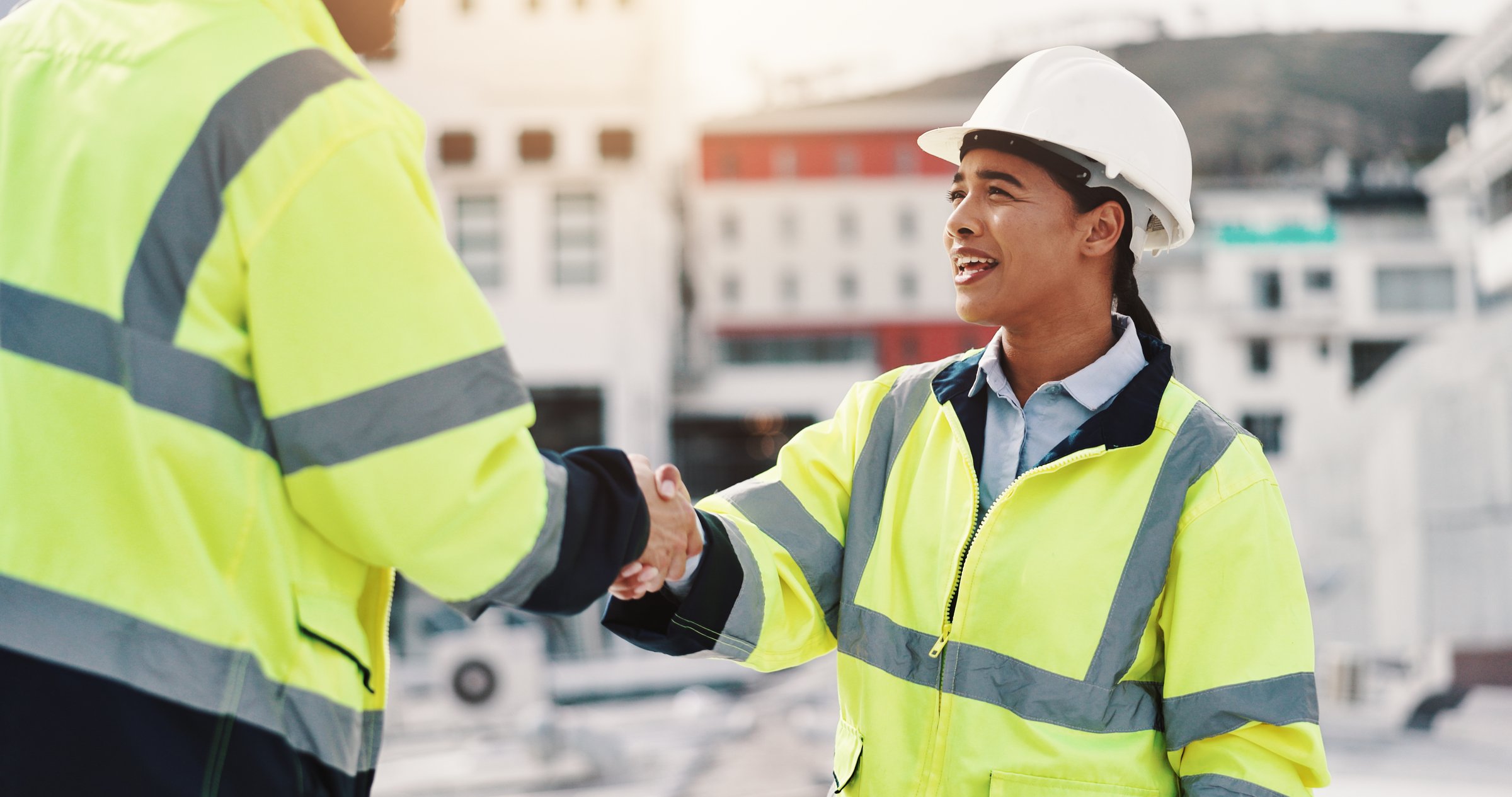 Construction, man and woman on building shaking hands for inspection, agreement or introduction in city. Civil engineering, contractor and technician on roof with handshake, deal or teamwork on site