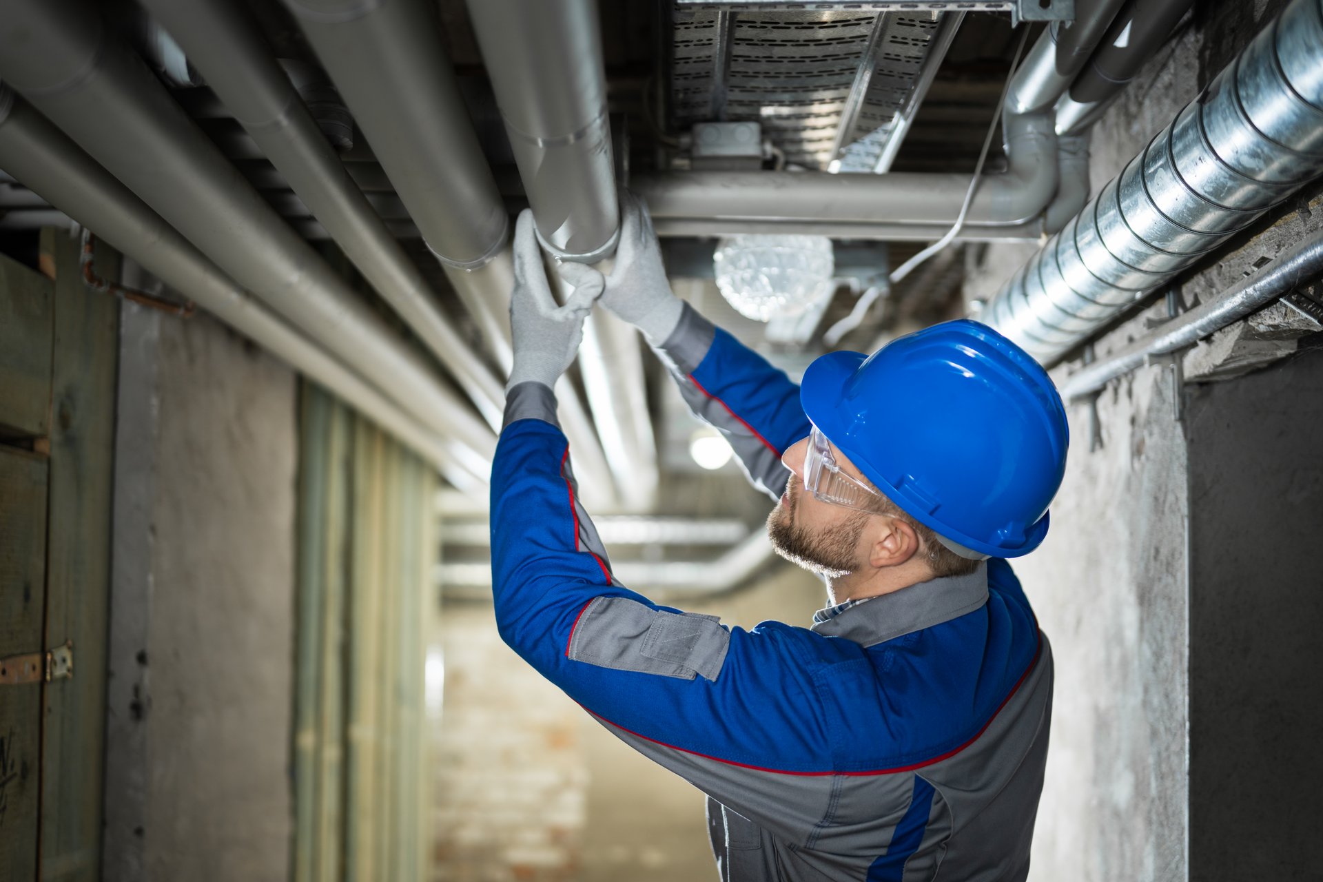 Male Worker Inspecting Water Pipes For Leaks In Basement