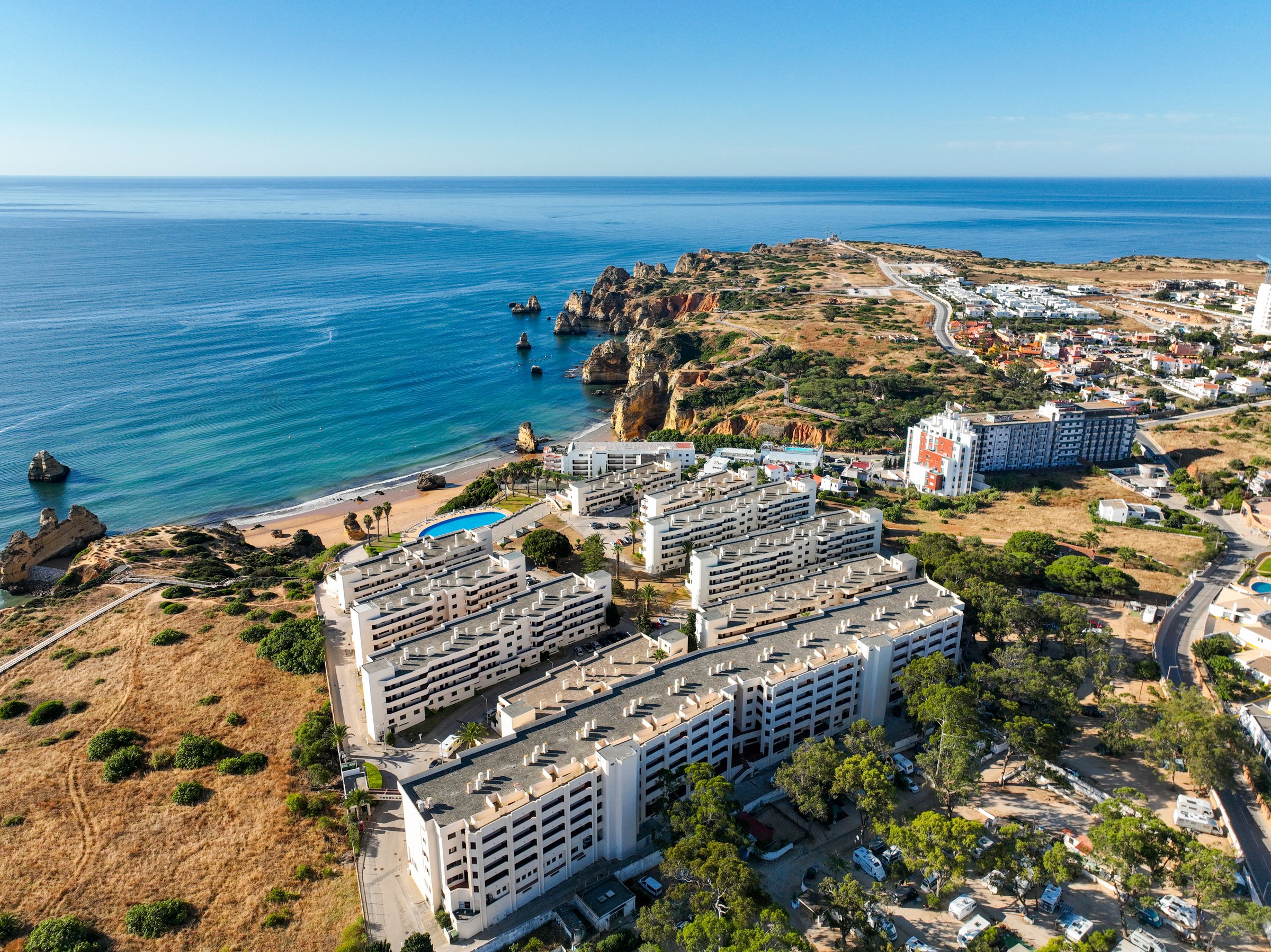 Coastal buildings near scenic Algarve cliffs and beach with deep blue ocean under clear skies