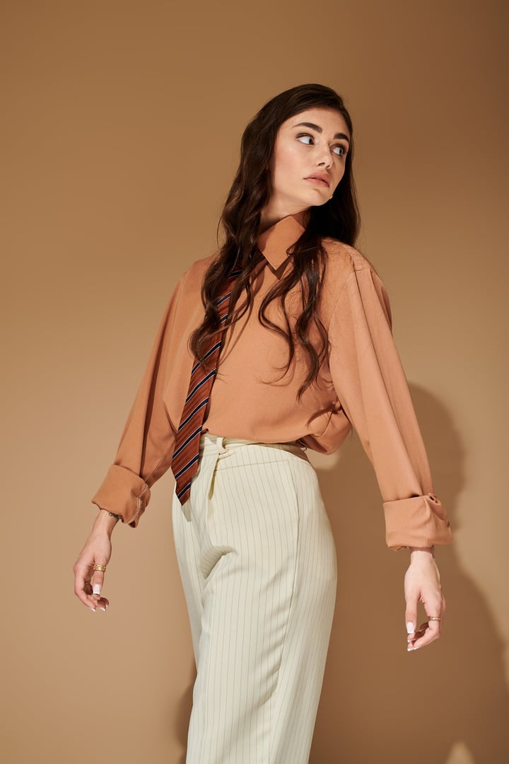 A young woman with long brown hair showcases her fashion sense in a stylish attire and tie.