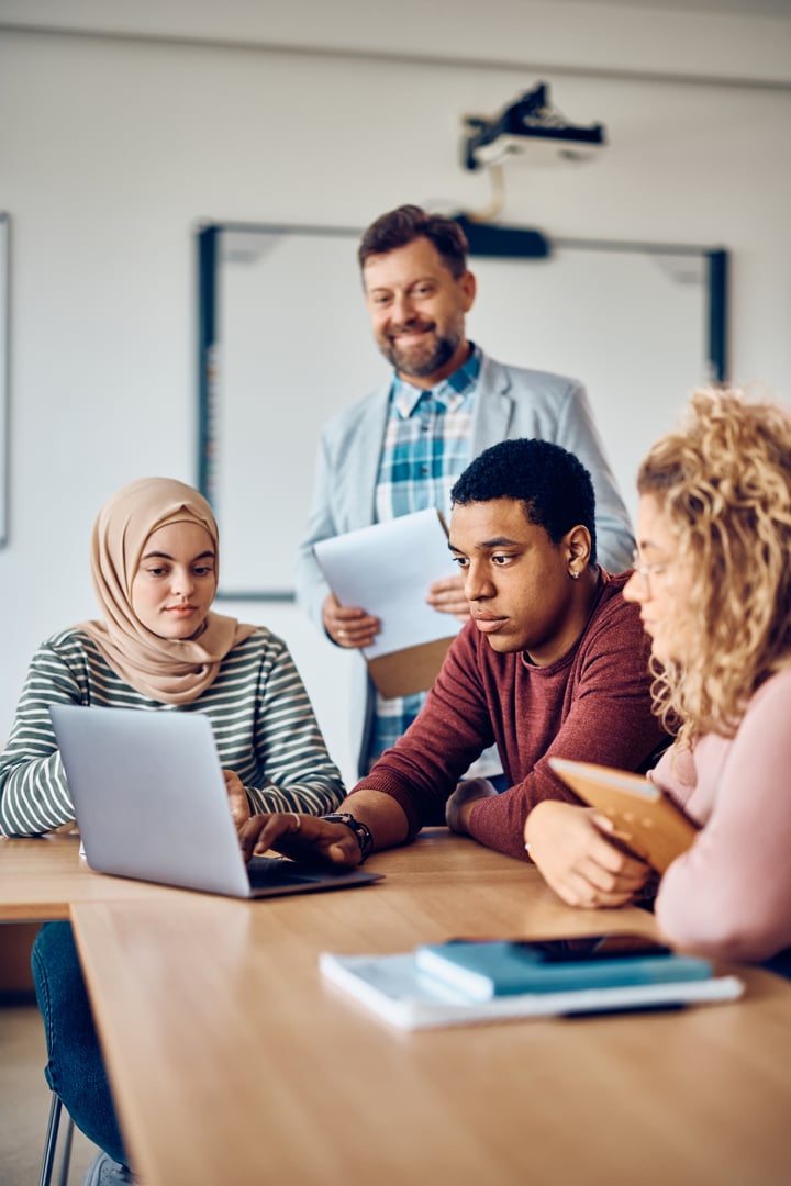 African American student and his college friends studying on laptop at college classroom.