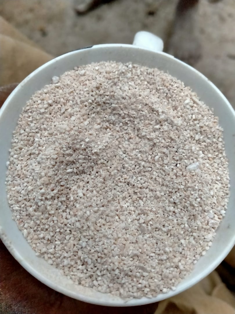 A close-up of a white cup filled with fine, light-colored granules, resembling sand or coarse salt.