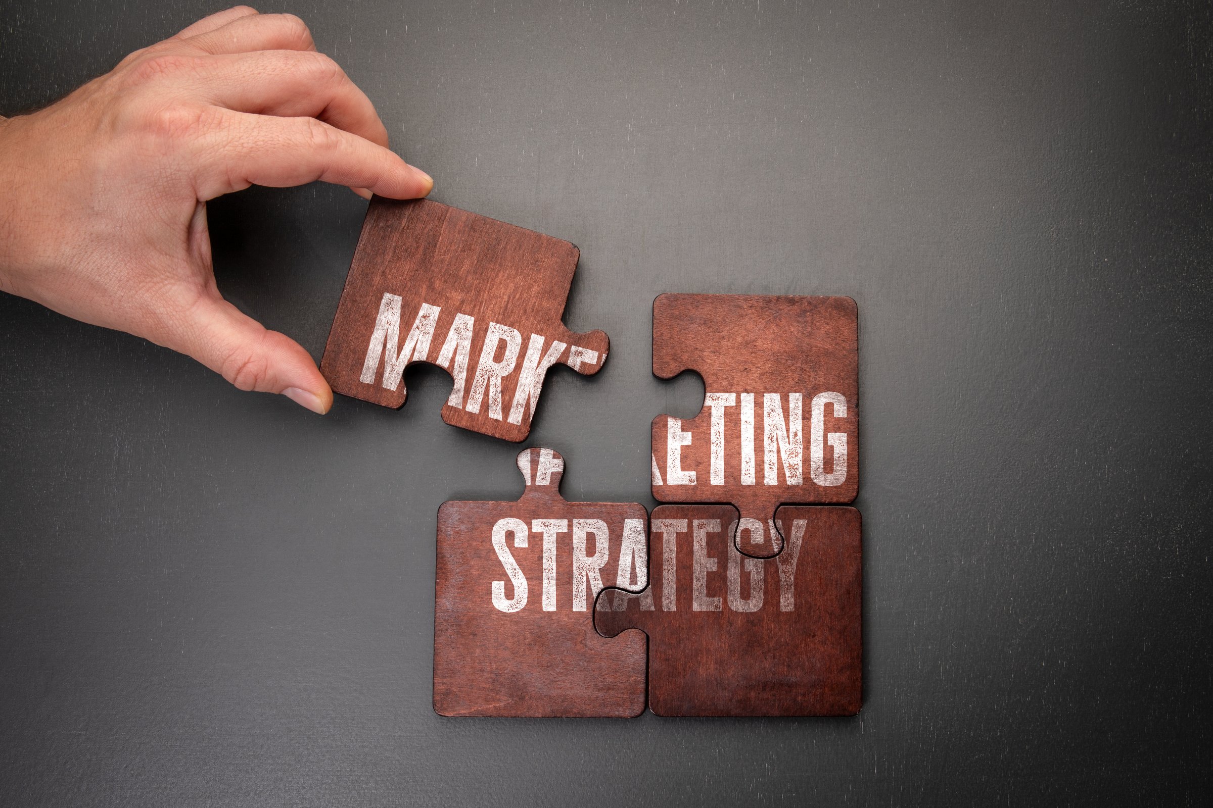Marketing strategy. Wooden puzzle pieces with text on a dark office table.