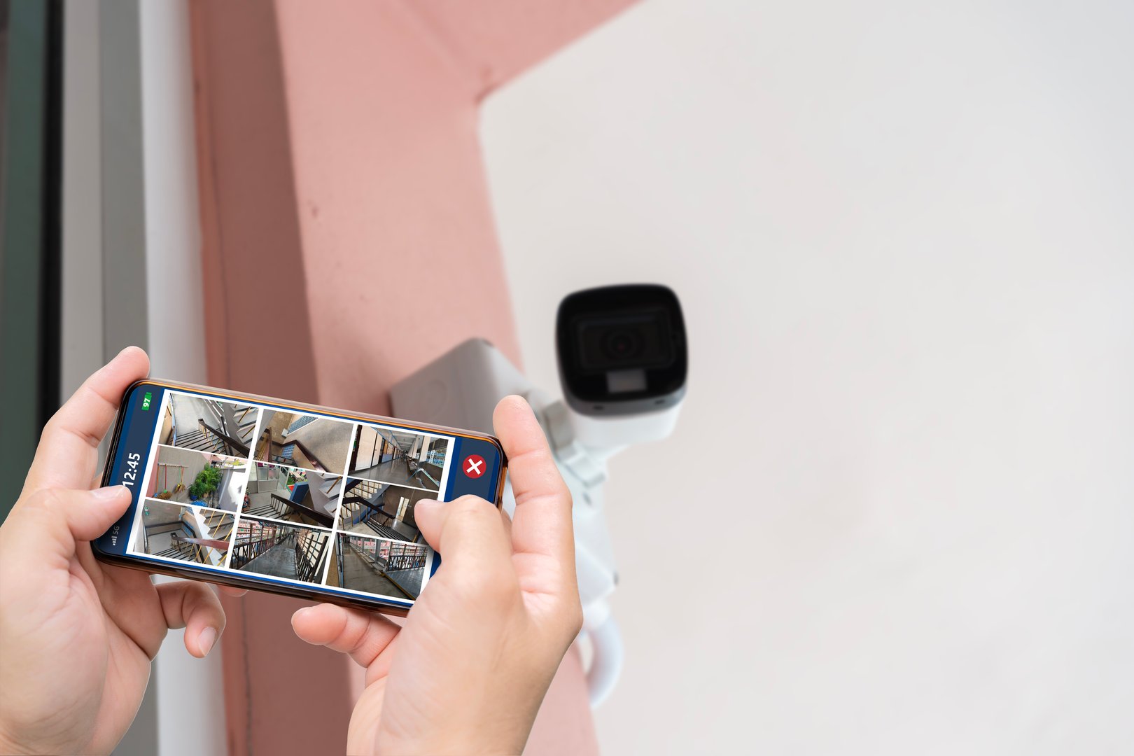 Professional cctv technician working. Person hand holding smartphone with multiple camera views of office locations. Surveillance, modern technology blurred background