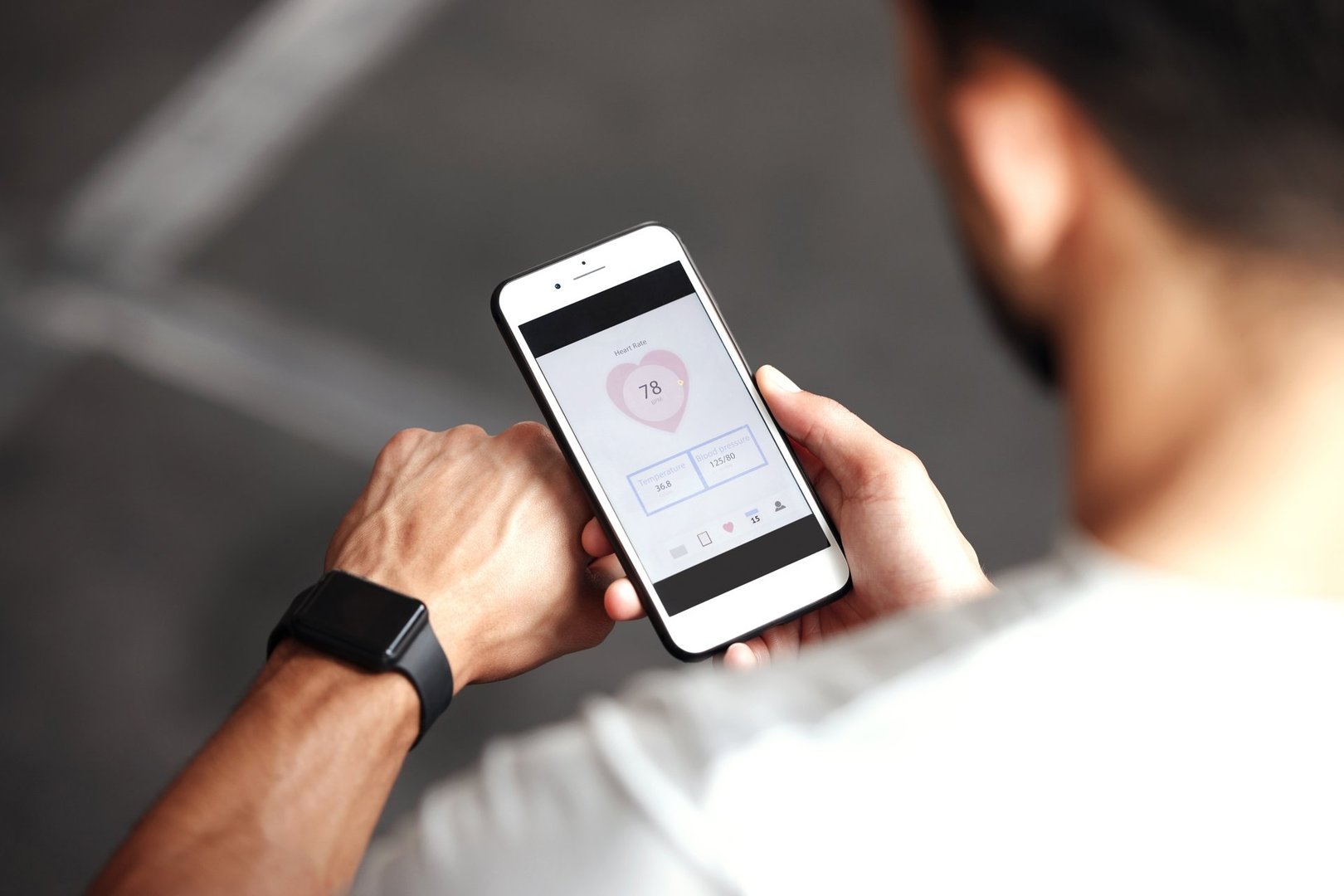 Closeup of one mixed race man checking health applications on digital wristwatch and cellphone for exercise in a gym. Guy from above wearing fitness tracker on arm and reading data about heart rate, body temperature and blood pressure on a phone screen