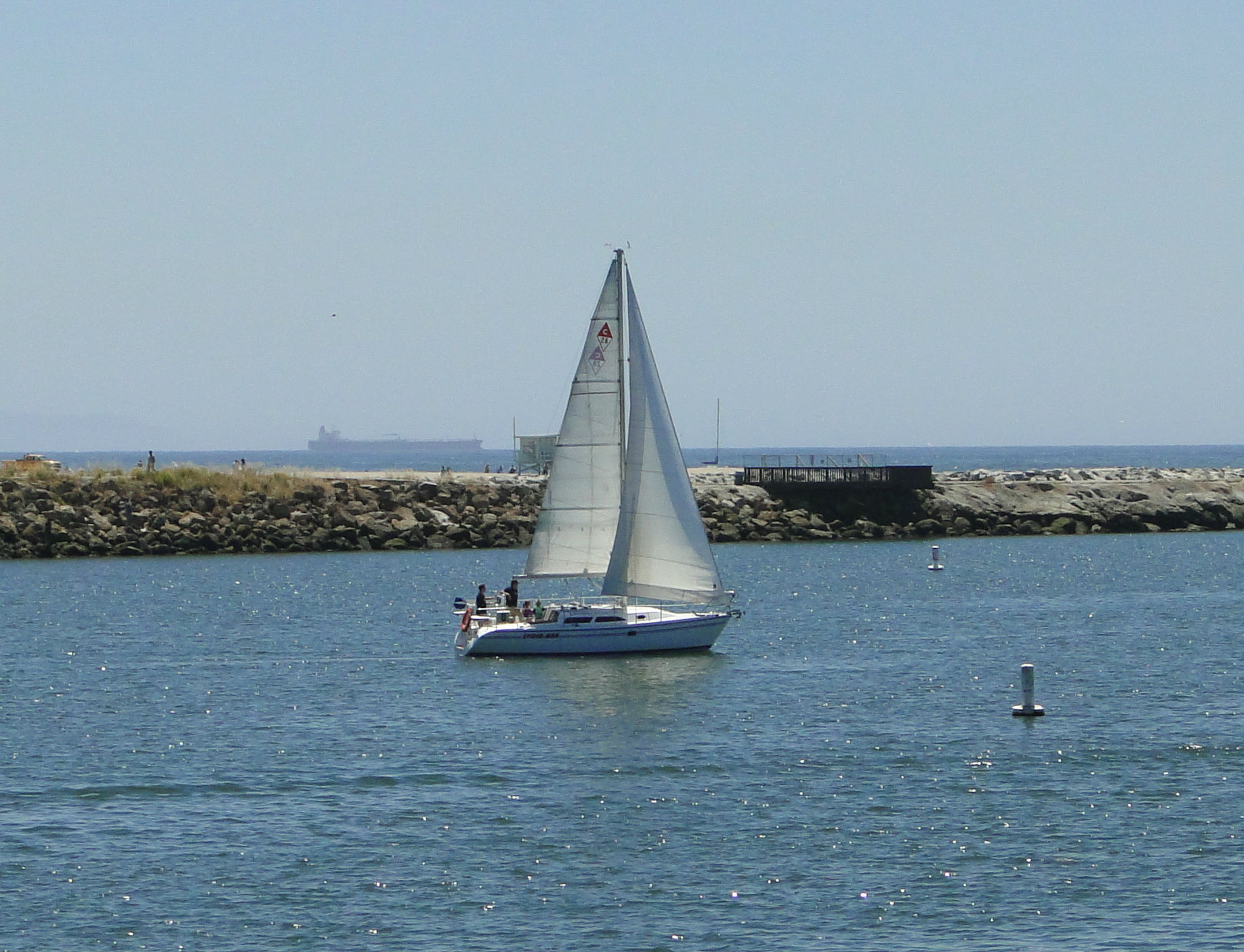 Sailboat in the Marina del Rey harbor channel surrounded by marina docks, boats, and waterfront condominiums in Los Angeles.