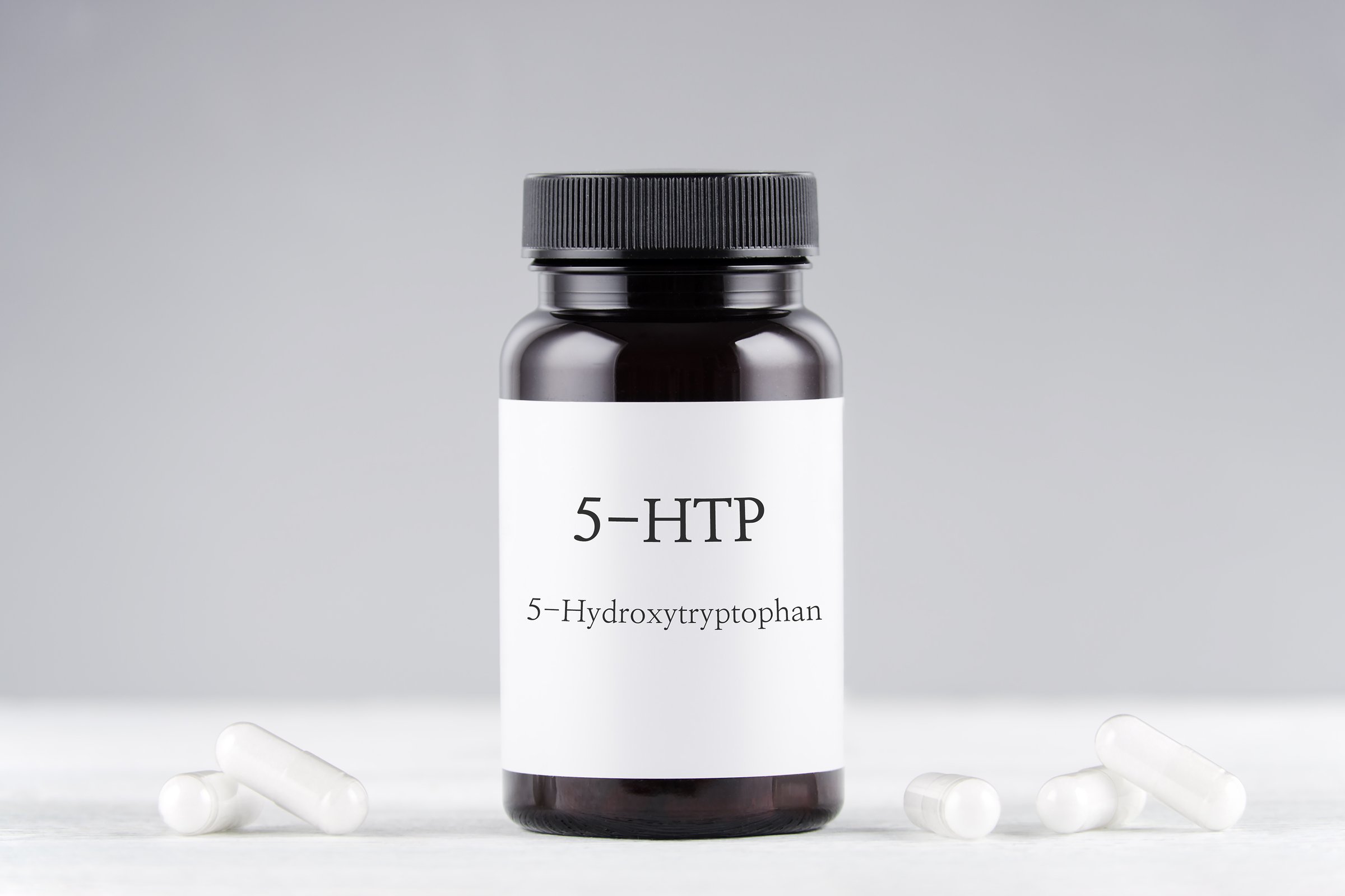 nutritional supplement 5-HTP hydroxytryptophan, bottle and capsules on gray background