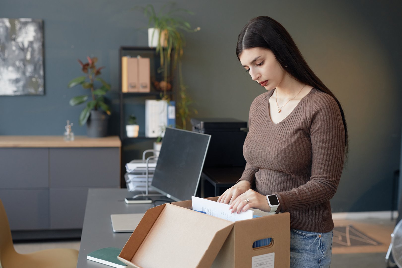 Side view portrait of young woman sorting through documents in folder box at office workplace, copy space