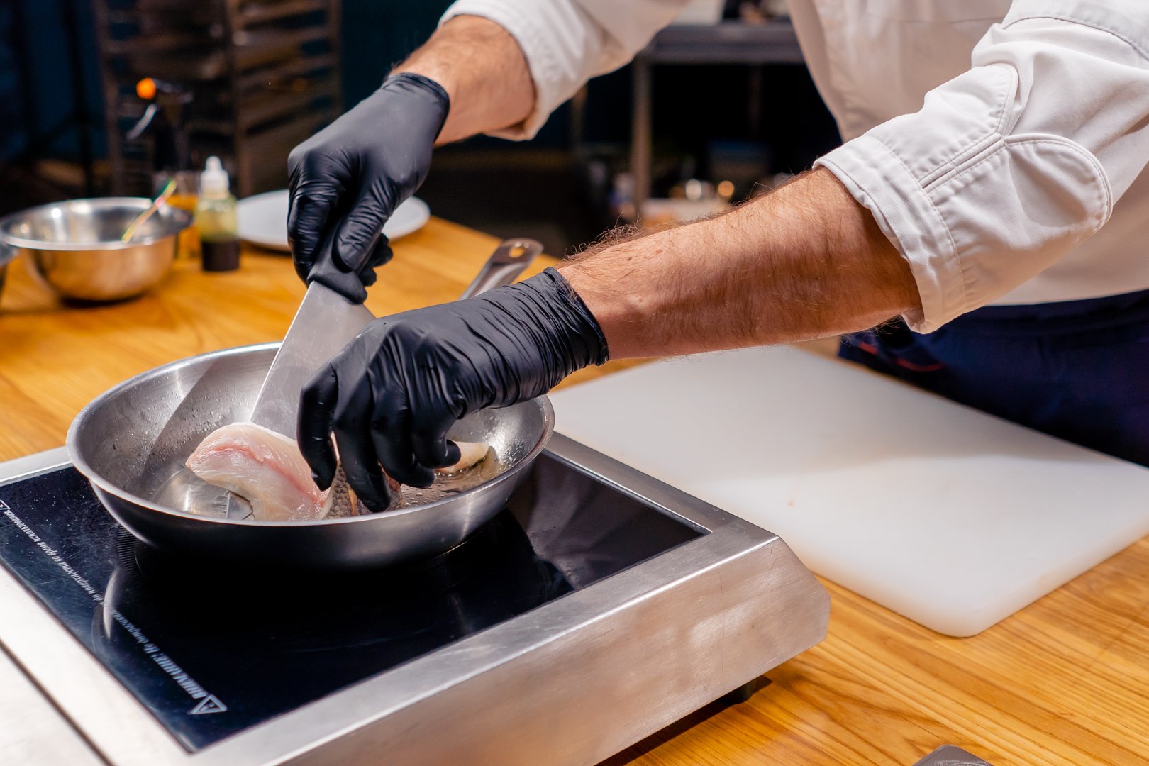 Chef profesional usando guantes de nitrilo negros biodegradables mientras prepara alimentos en una cocina