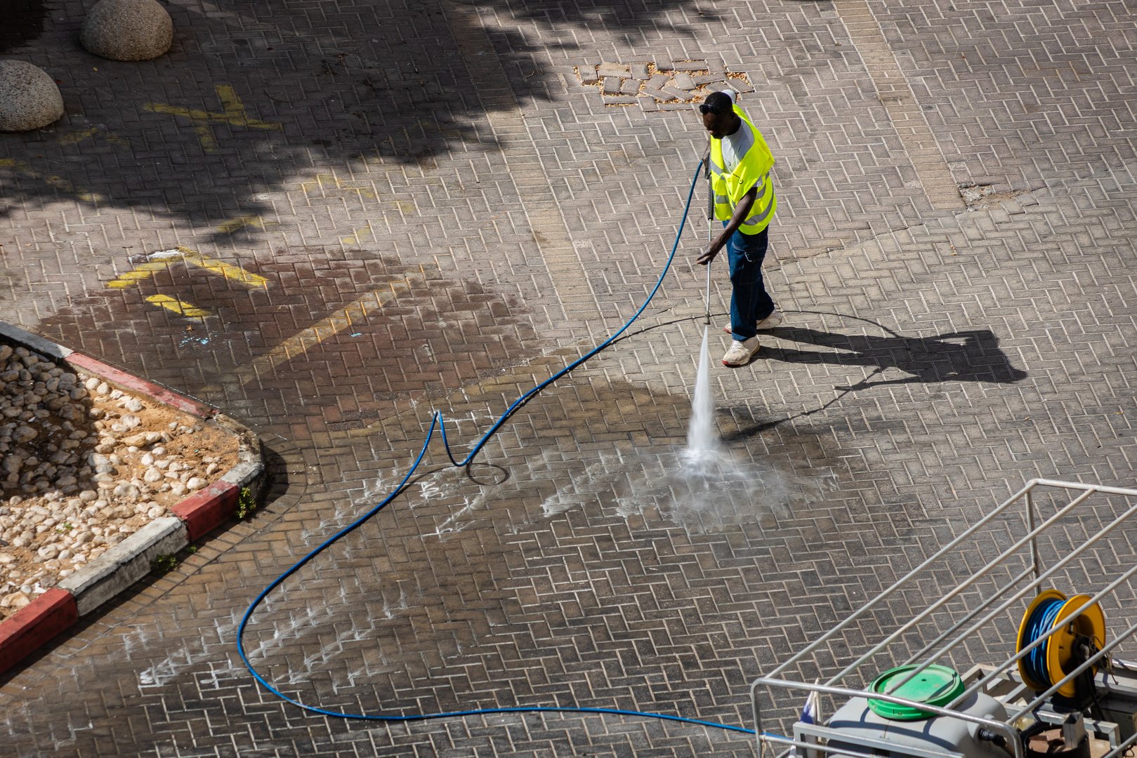 Eilat, Israel - July 9, 2024: Municipal worker in high visibility vest sinitizes garbage cans area. Different colors trash containers for sorting garbage. Cleaning company's name in hebrew on man's vest