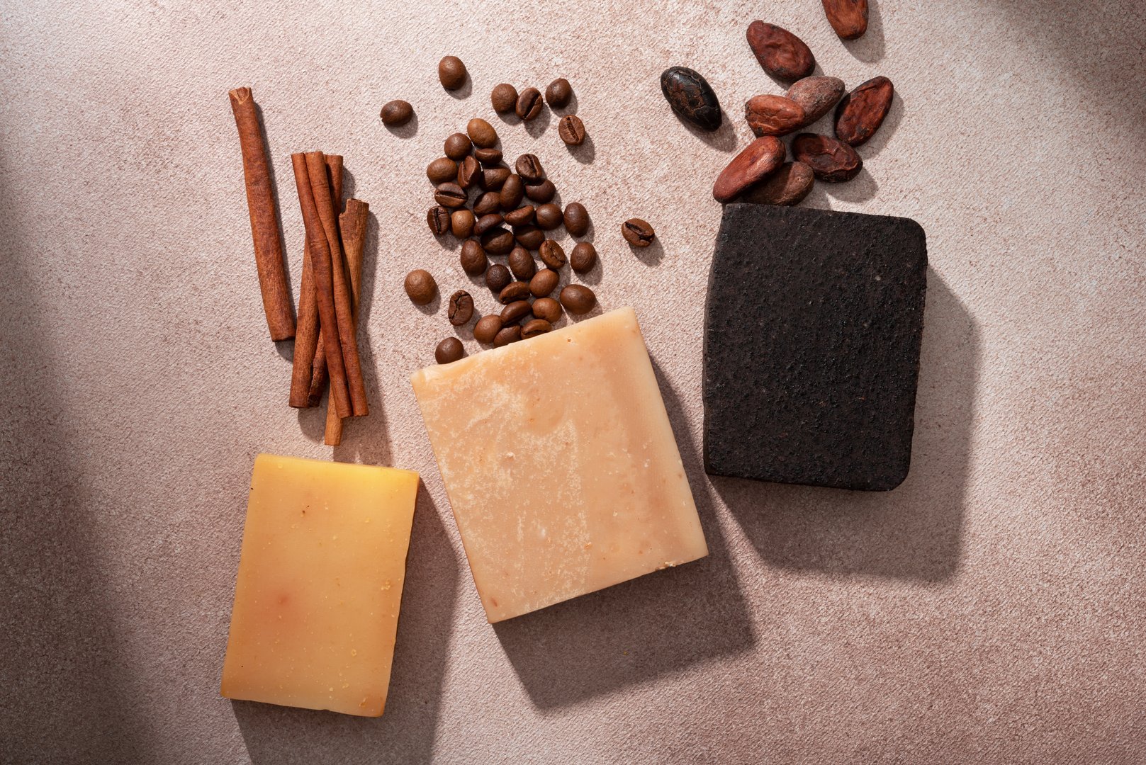 Handmade natural soap bars with coffee beans, cocoa beans and cinnamon sticks on a textured background. Organic skincare concept for beauty, wellness, and sustainable self-care products.