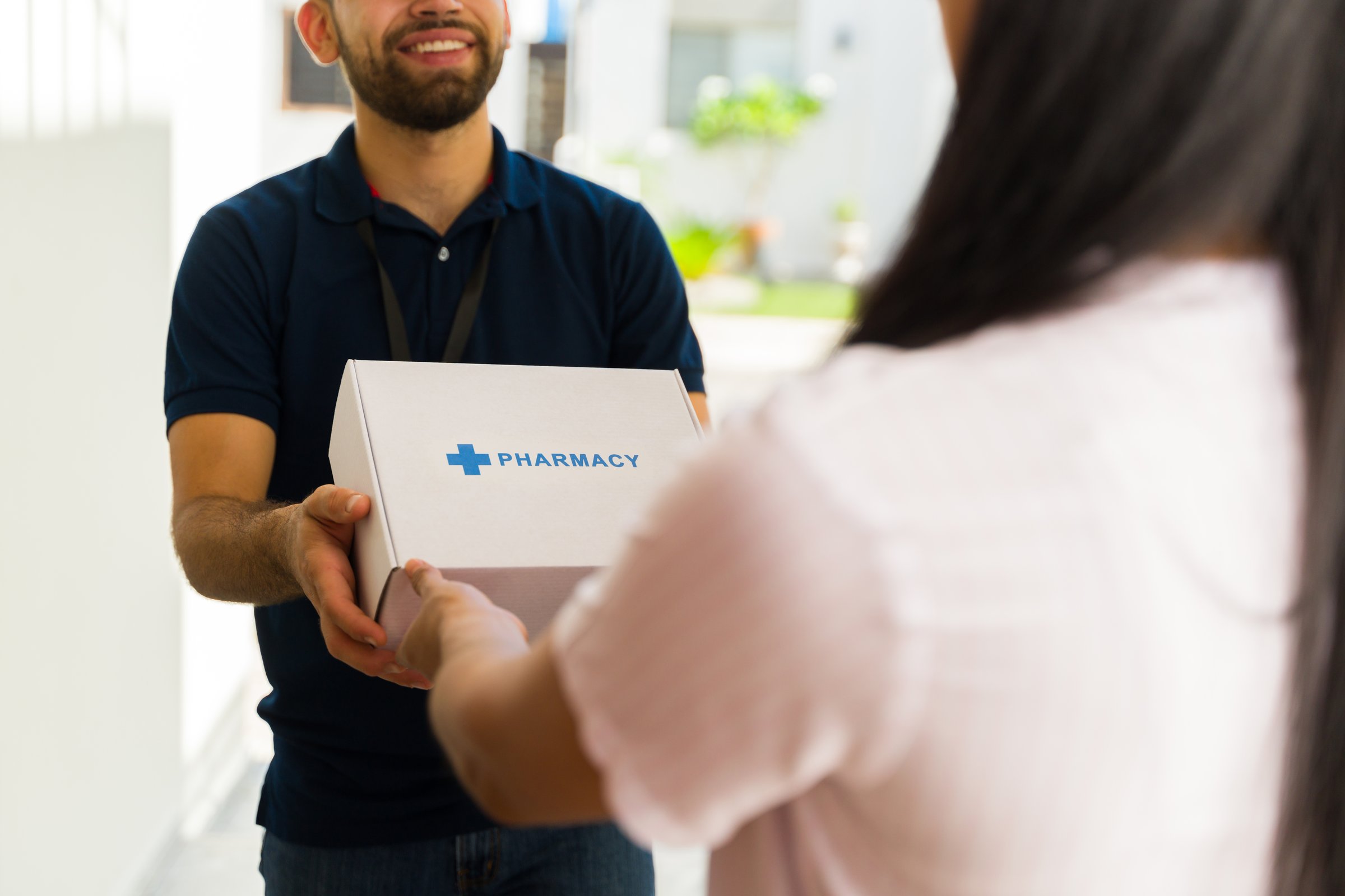 Smiling delivery man holding a white box with the word pharmacy on it while delivering medication to a woman