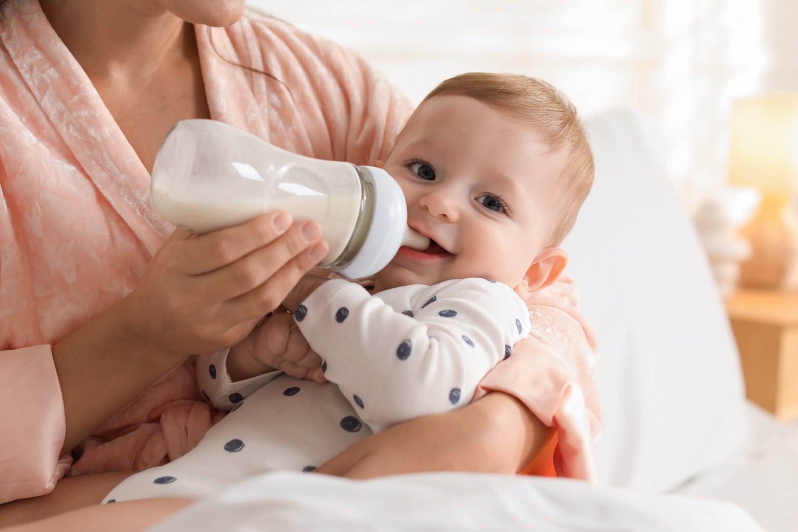Mother feeding her little baby from bottle on bed at home, closeup