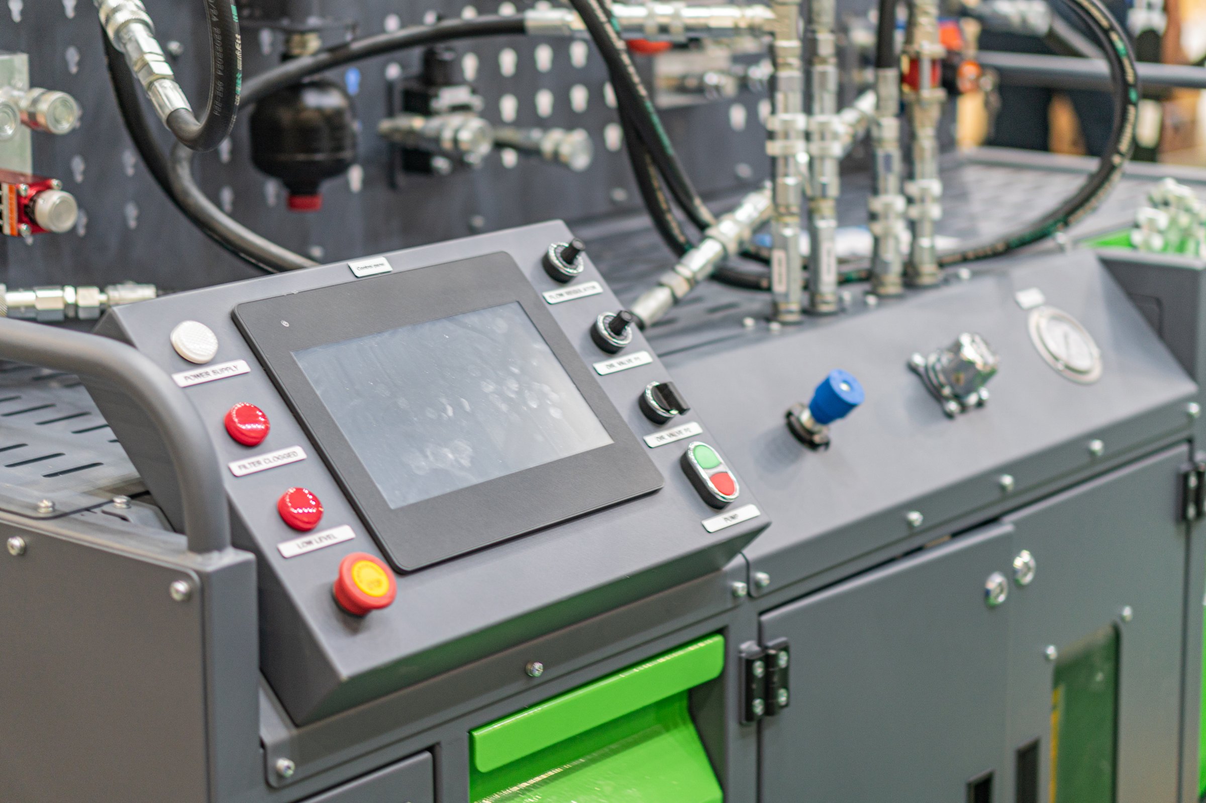 Industrial setting with two machines, one green and the other silver, likely part of a manufacturing line Focused control panels, hoses, cables, and complex functionality Artificial lighting, harsh