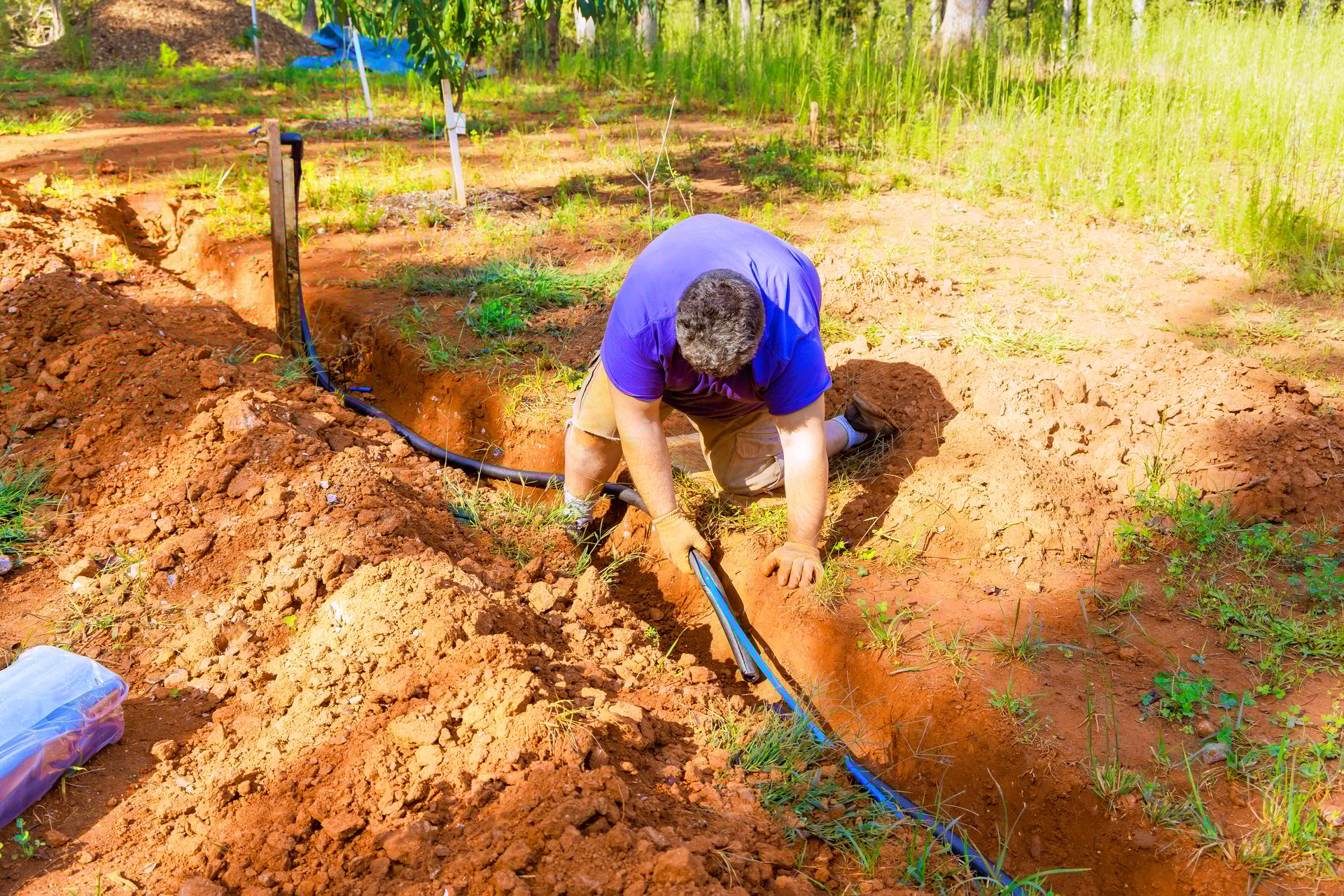 Worker in garden, digging, installing PVC water pipe for new irrigation system in rich, brown soil