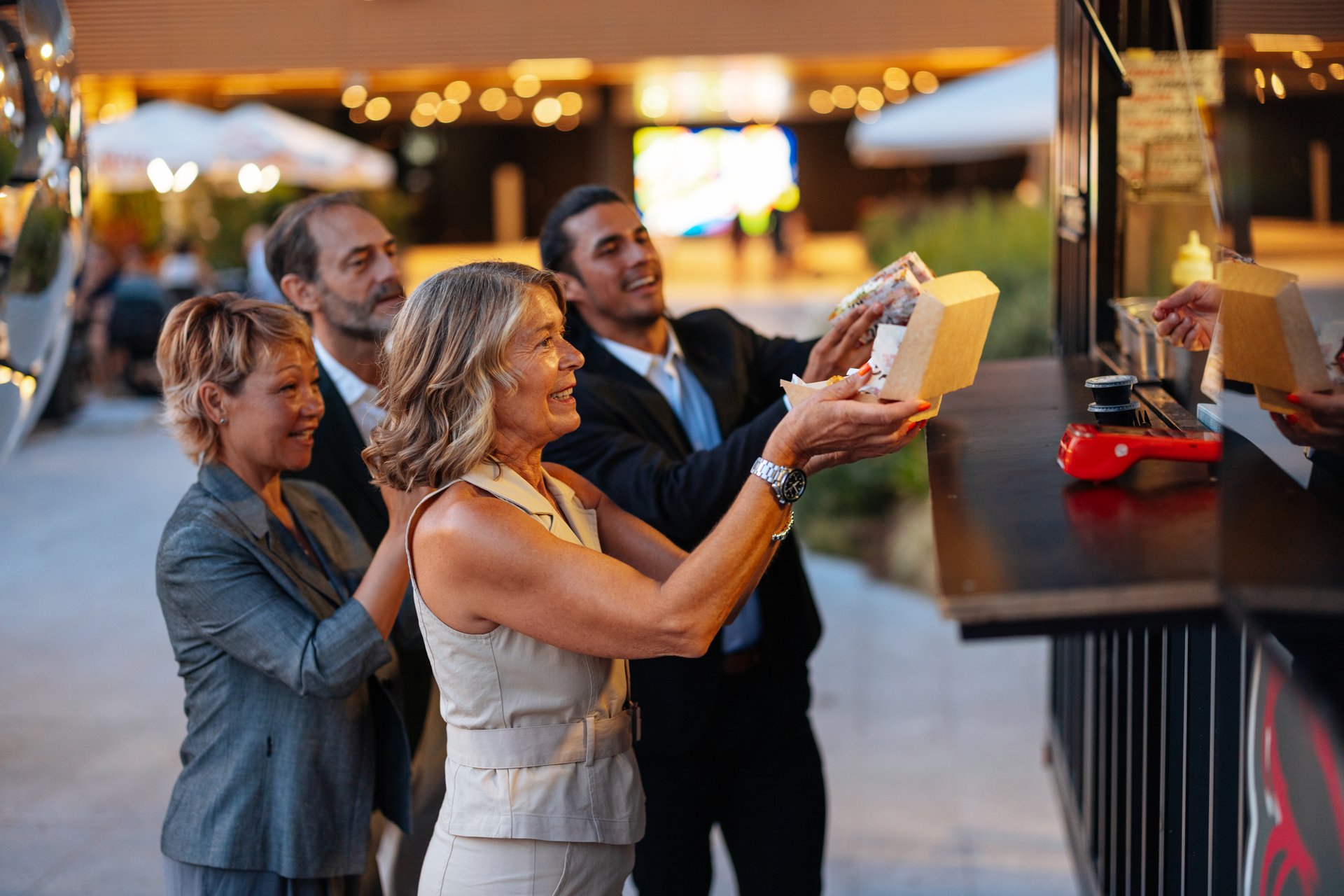 Group of colleagues enjoying a lively lunch break, savoring delicious takeaway from a vibrant food truck in the bustling city
